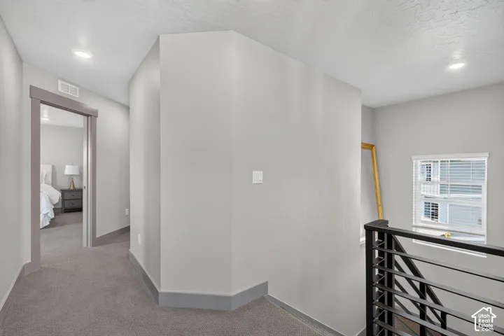 Carpeted hallway with recessed lighting, trim details, and a modern stair railing