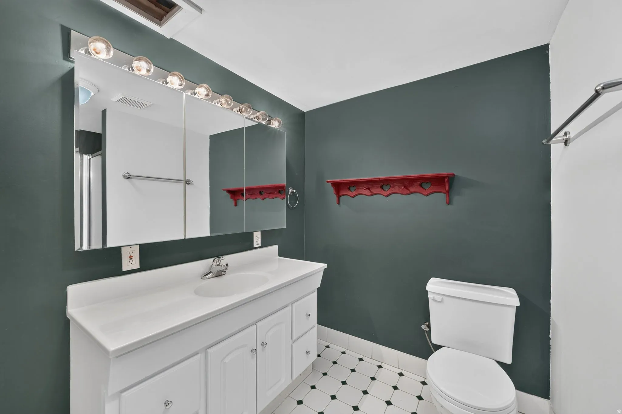 Bathroom featuring a white vanity with integrated sink, a large mirrored medicine cabinet with vanity lighting, and a white toilet