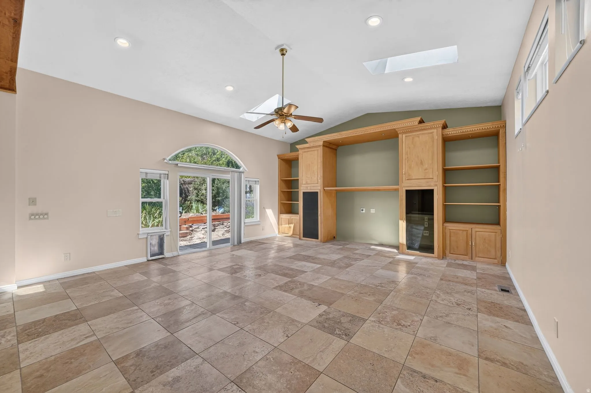 Spacious room featuring large format tile flooring, a vaulted ceiling with skylights, recessed lighting, and a ceiling fan
