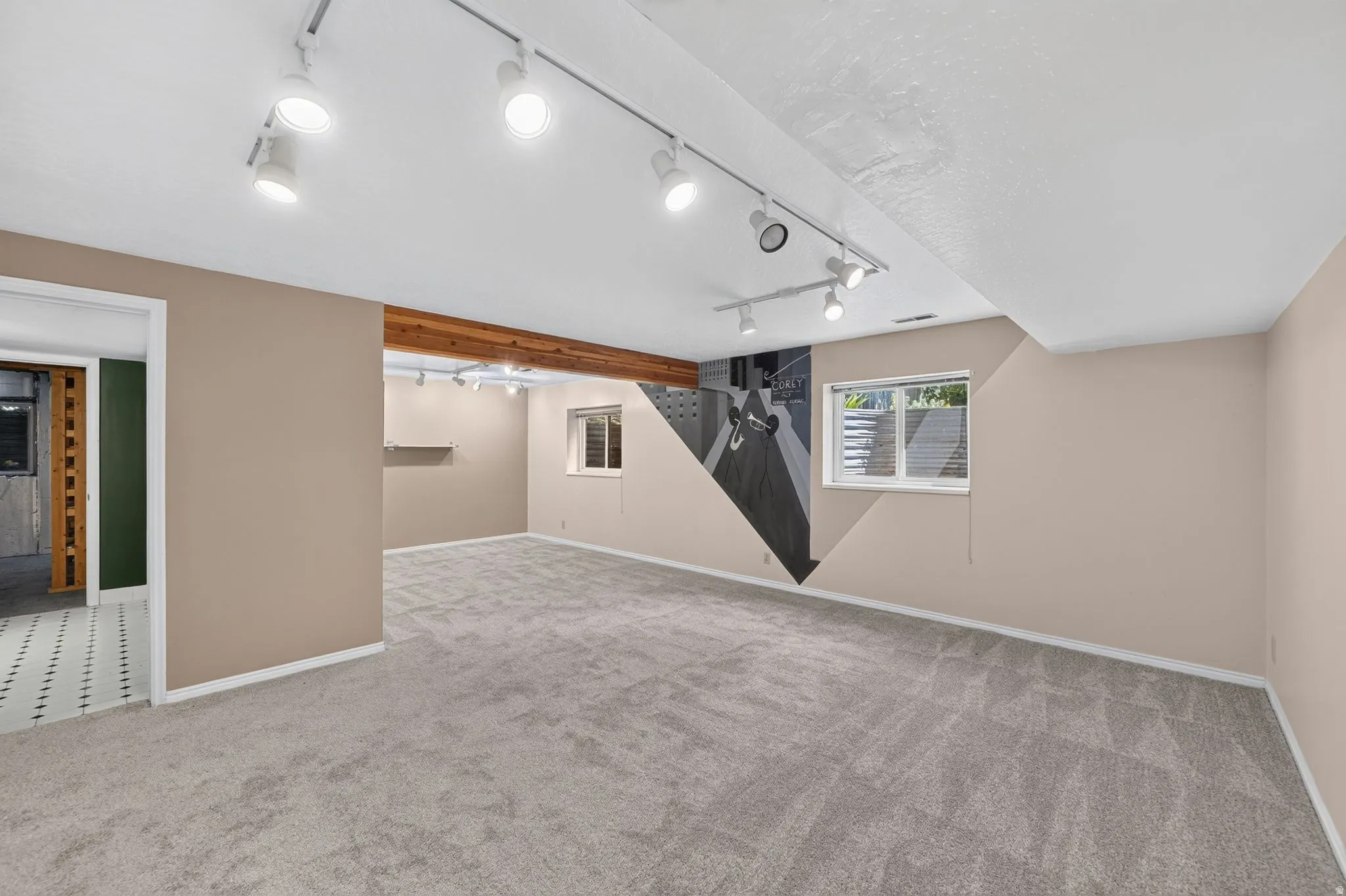 Expansive carpeted room featuring track lighting and a natural wood beam