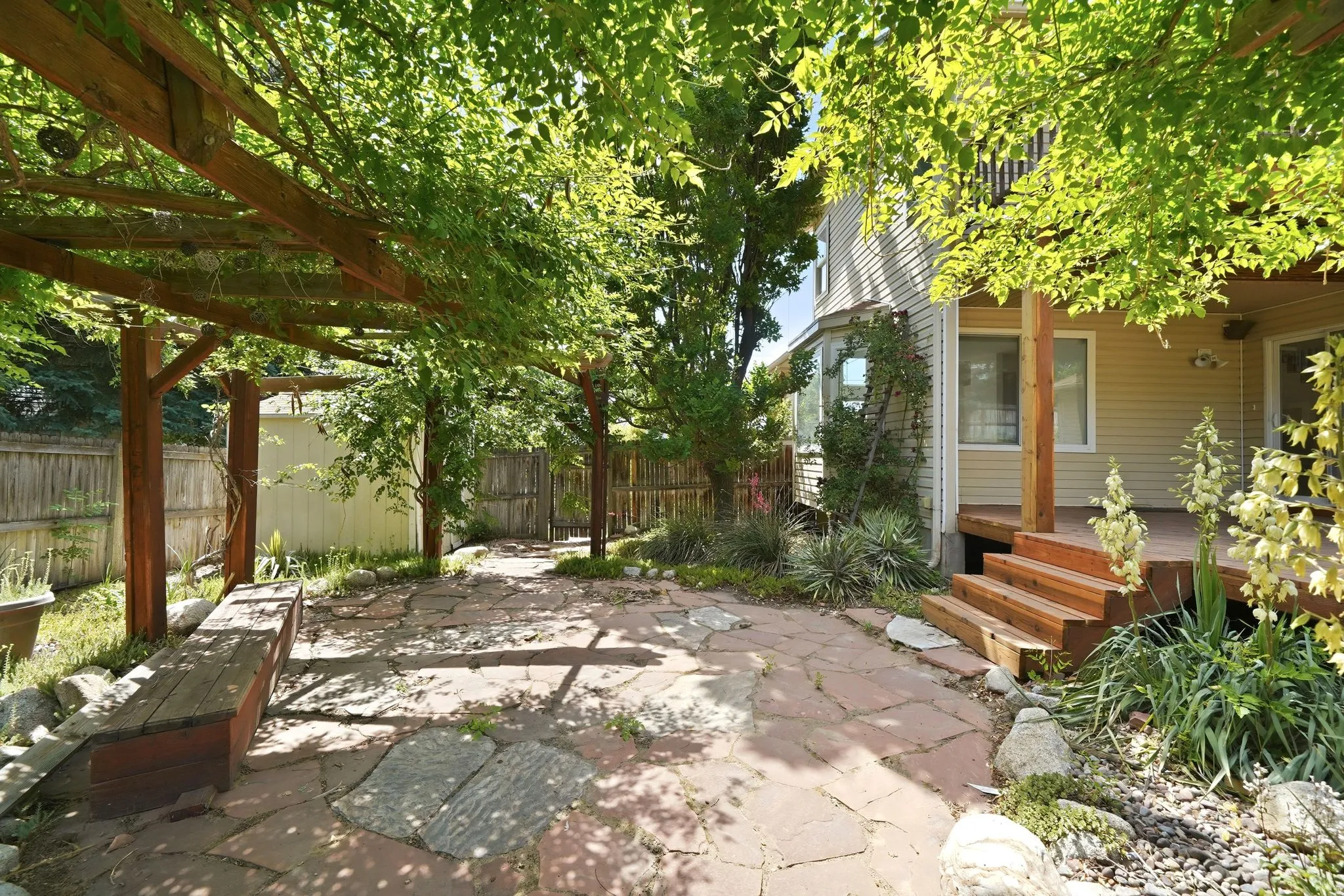 Flagstone patio with an overhead wood pergola, providing dappled sunlight