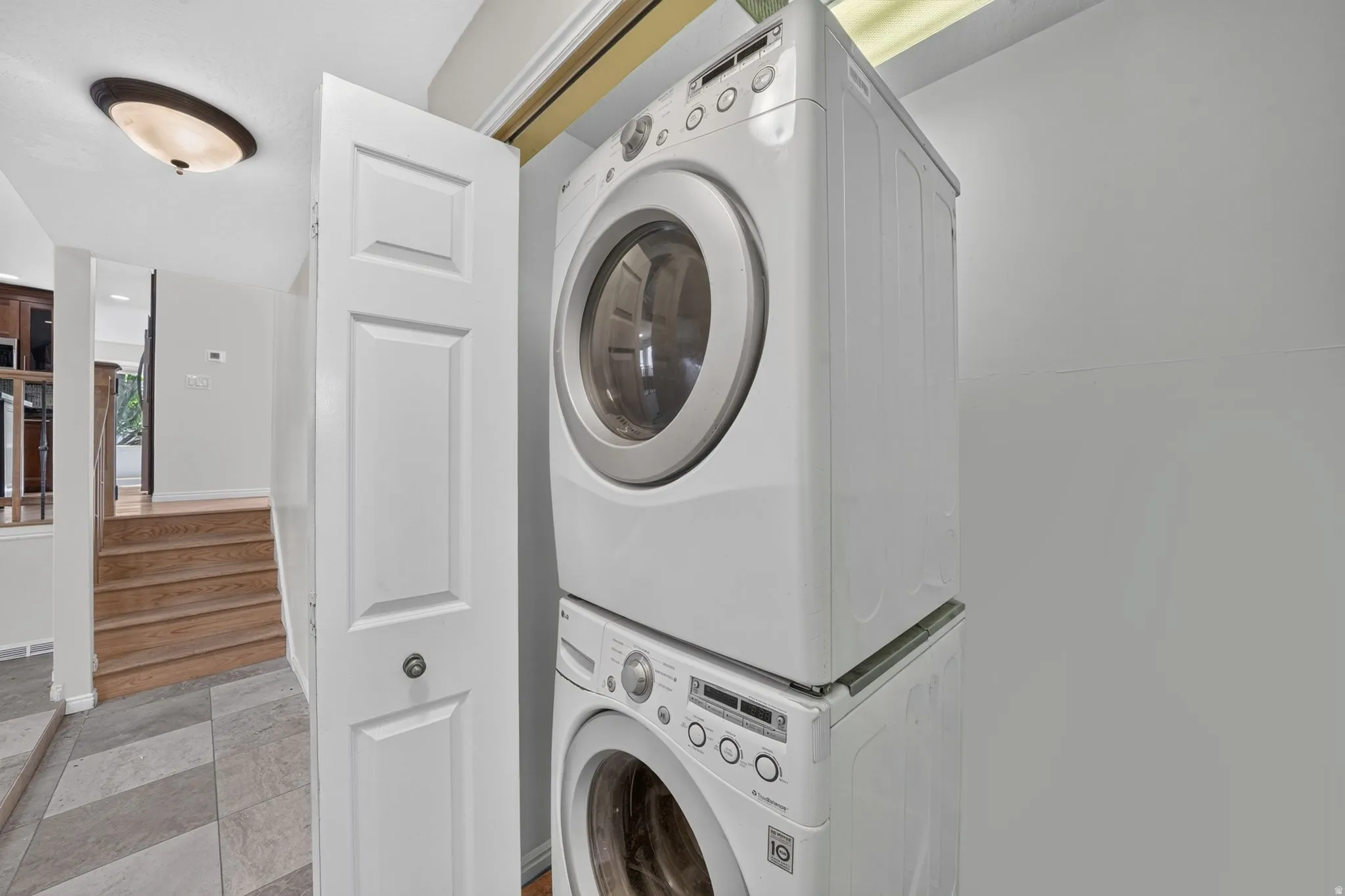 Laundry area featuring a stacked washer and dryer, adjacent to a hallway with wood-finish stairs and gray tile flooring