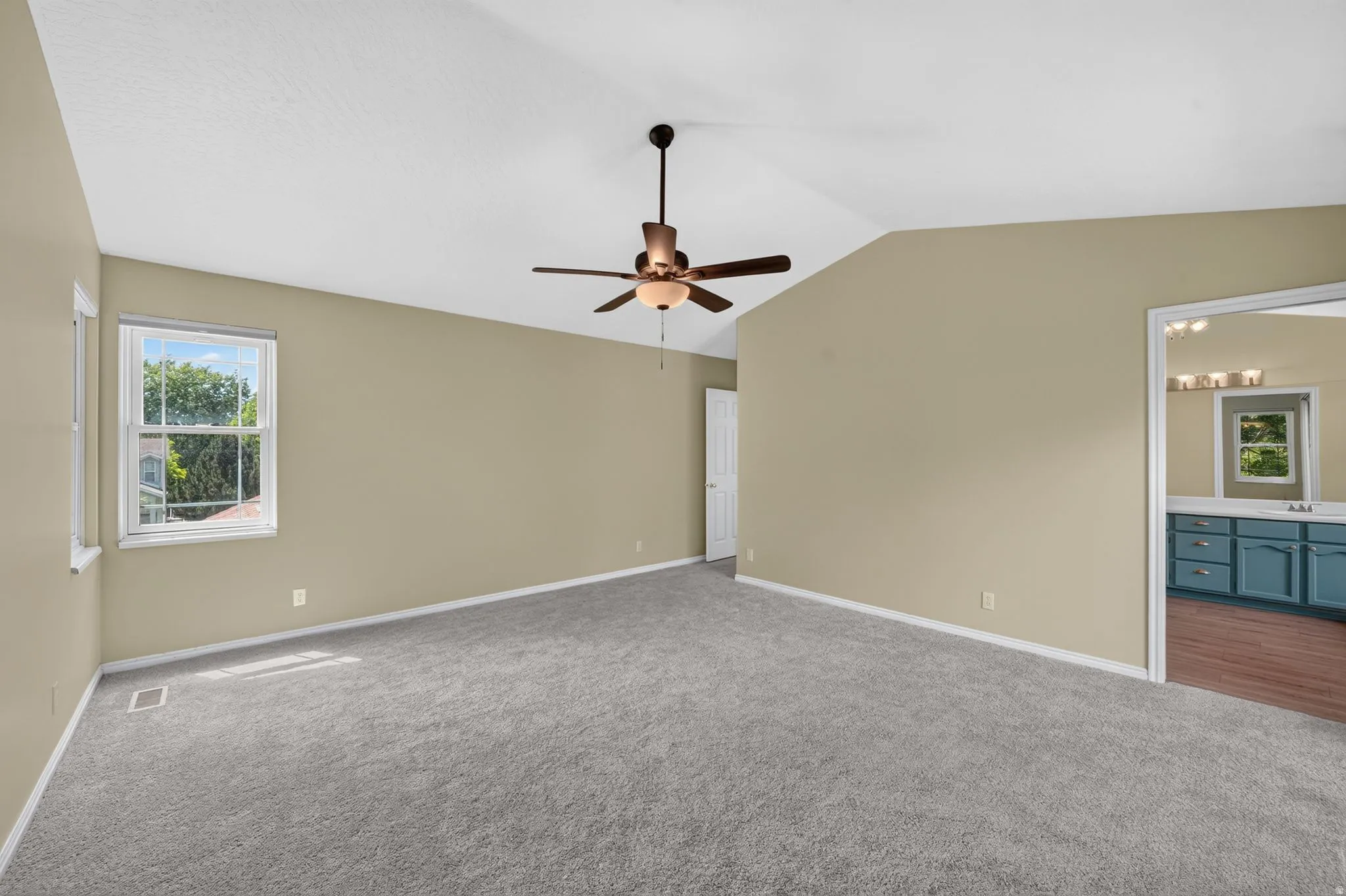 Spacious room featuring vaulted ceilings, neutral-toned walls, and grey carpeting