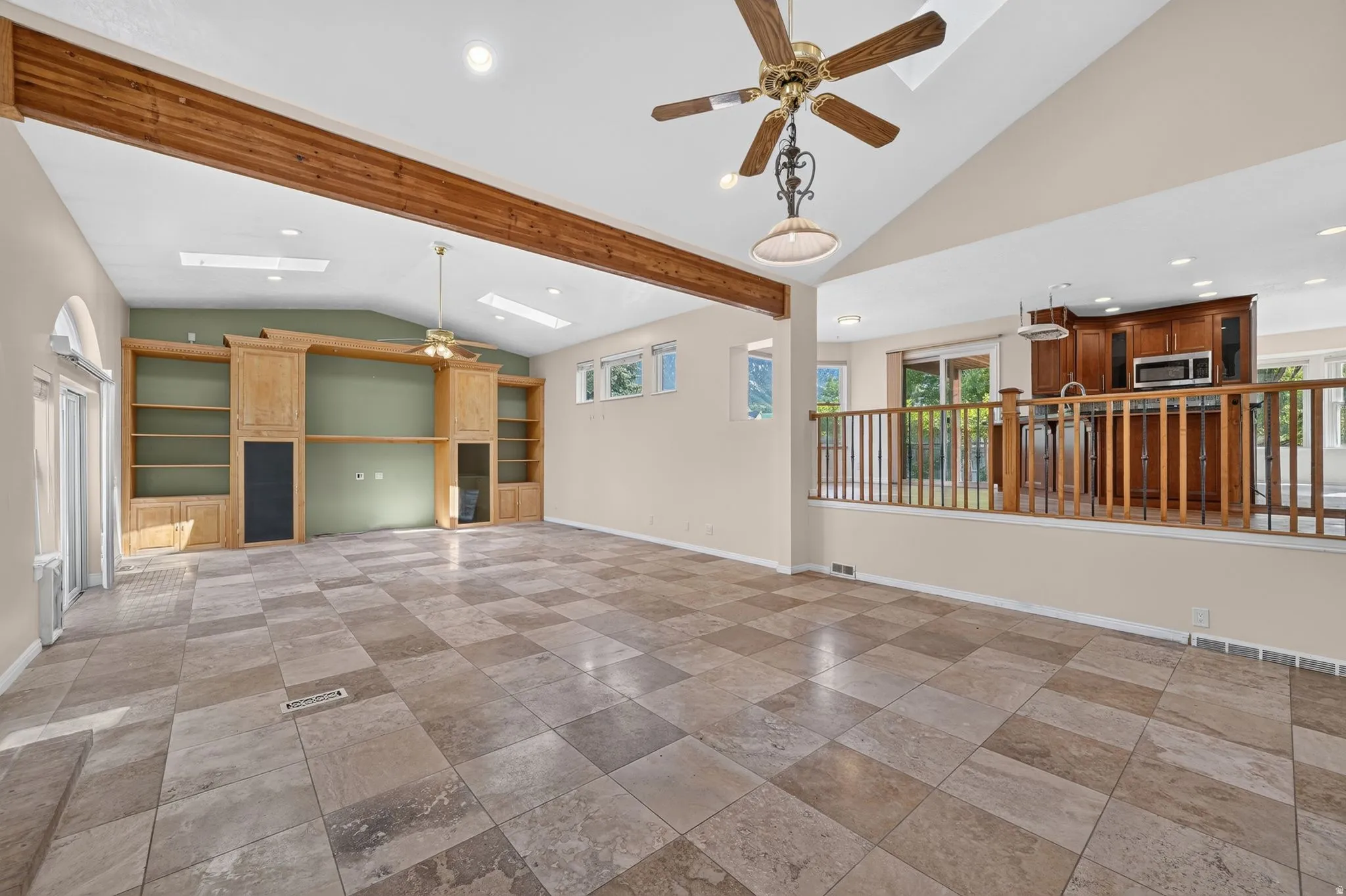 Spacious room featuring vaulted ceilings with exposed wood beams, skylights, and ceramic tile flooring