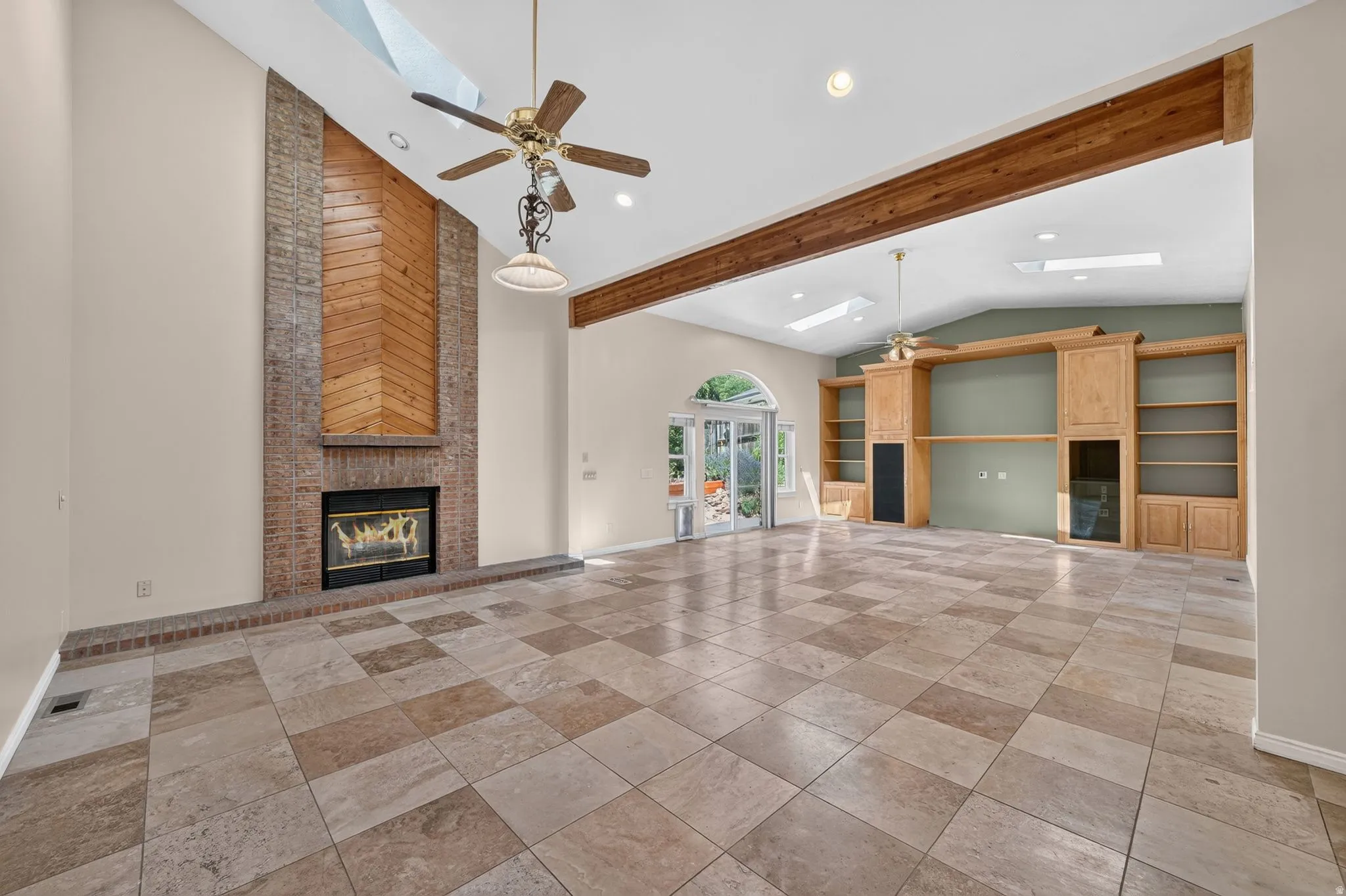 Spacious interior featuring checkerboard tile flooring, a prominent brick fireplace with wood paneling, and an expansive built-in entertainment center with shelving