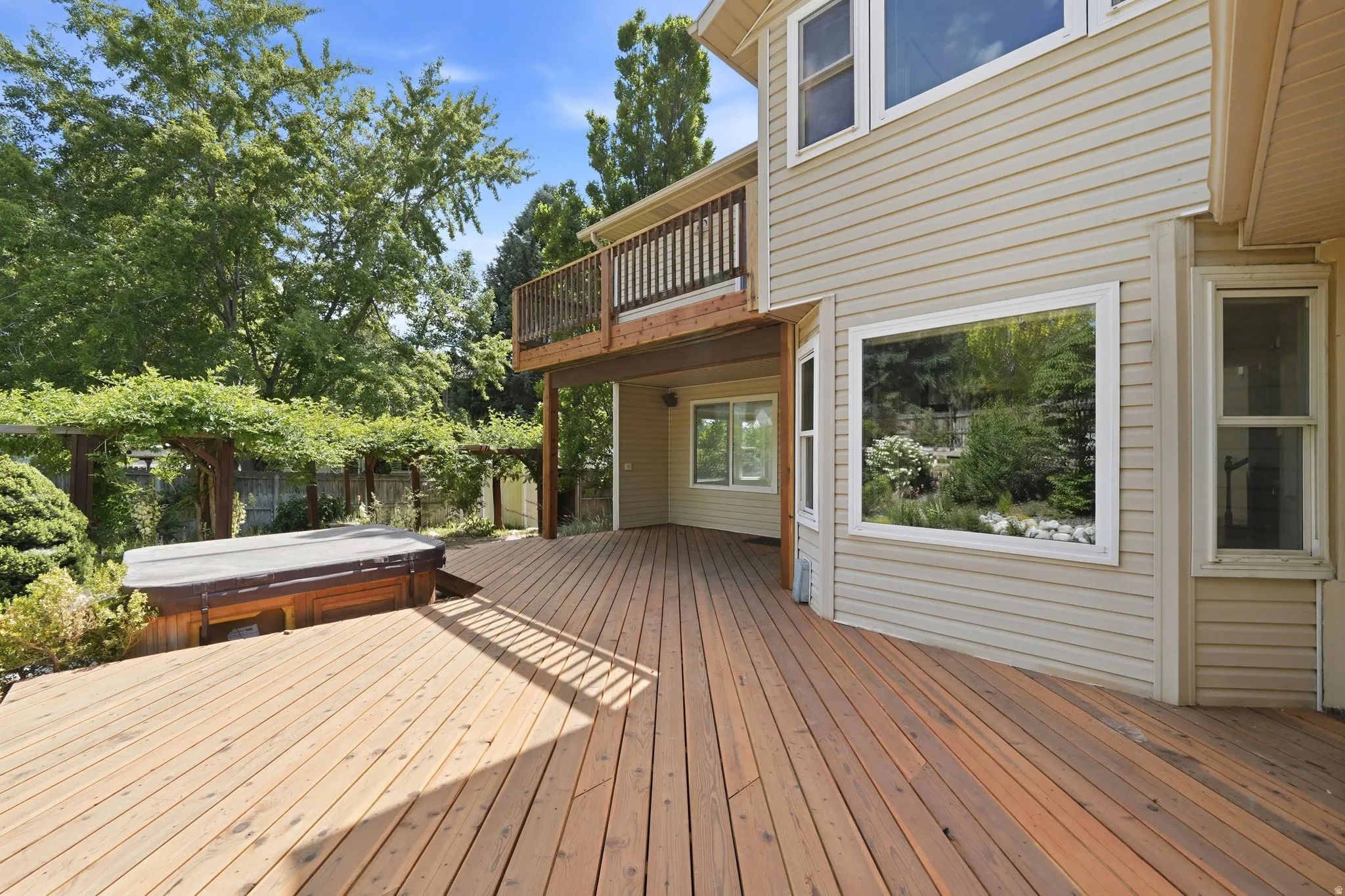 Expansive wood-finish deck with an integrated hot tub and an overhead pergola