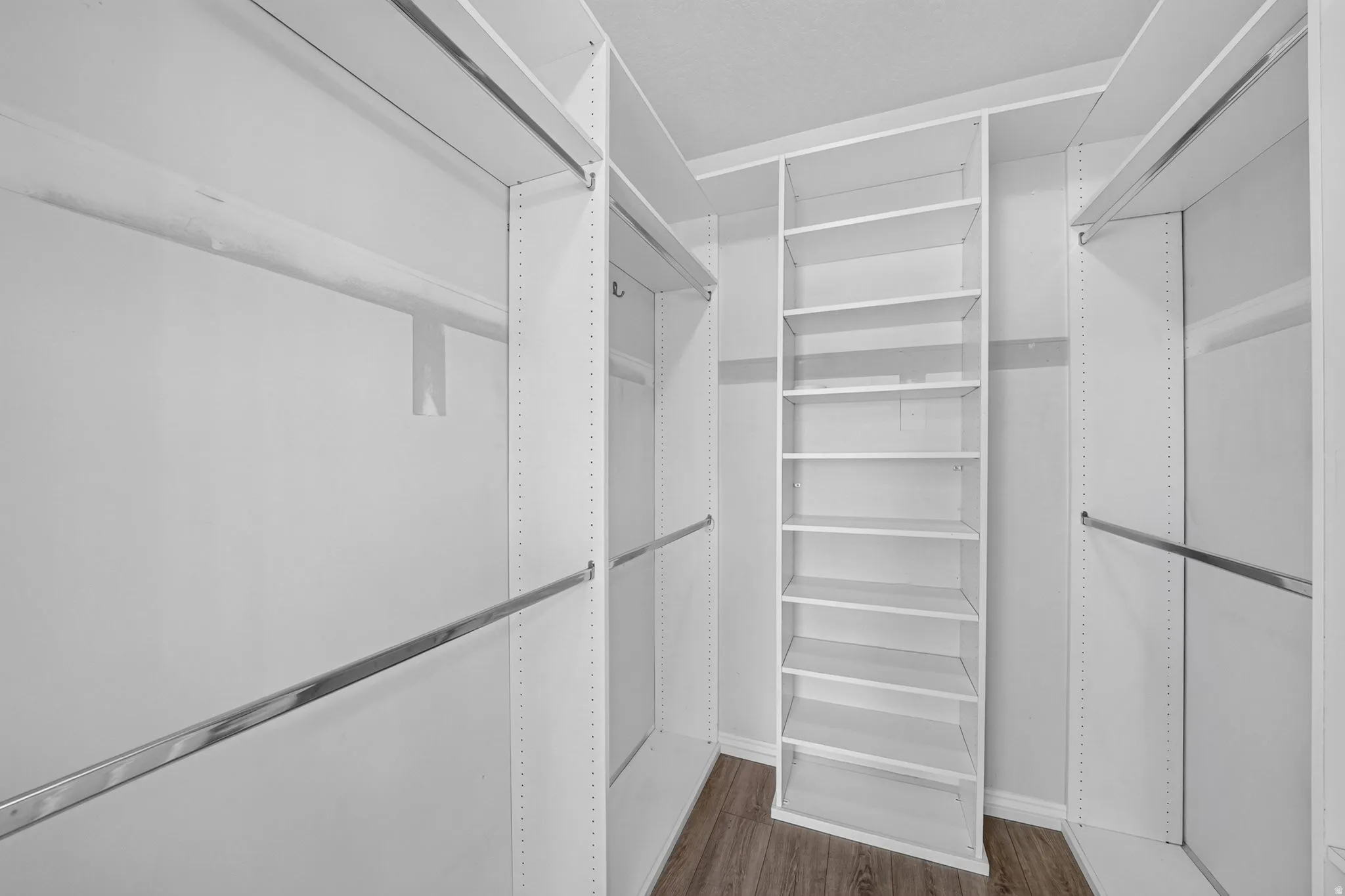 Custom closet system with extensive white shelving, multiple hanging rods, and wood-finish flooring