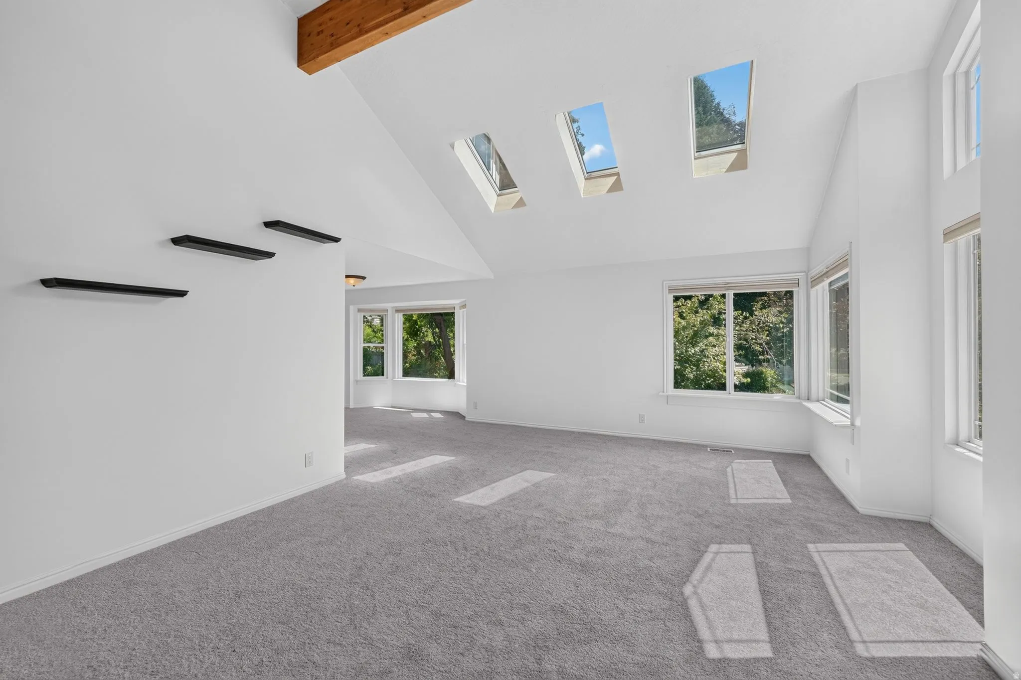 Spacious room featuring vaulted ceilings with exposed wood beams, three skylights, and light gray carpet