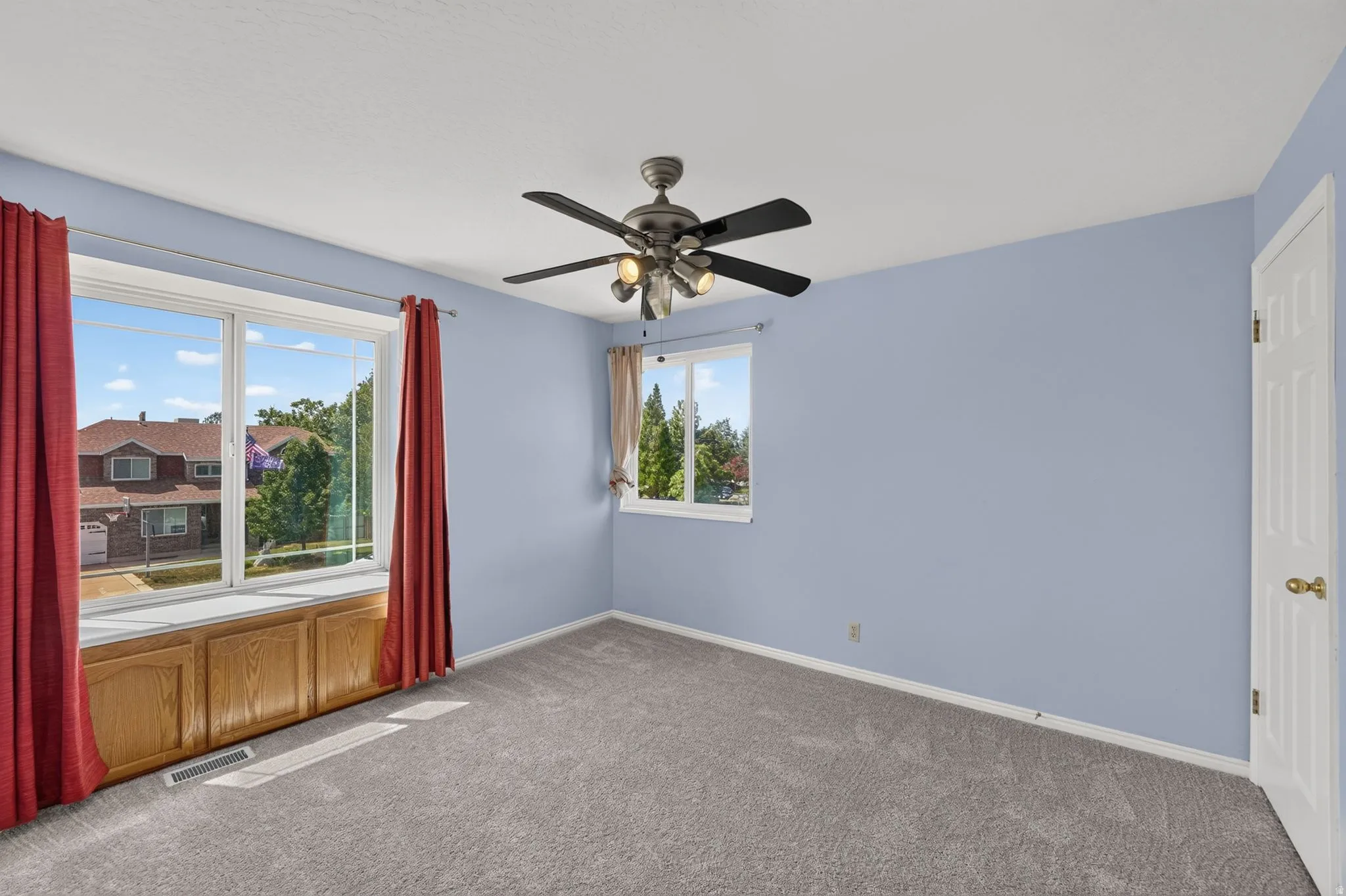 Spacious room featuring light blue walls, gray carpet, and two windows