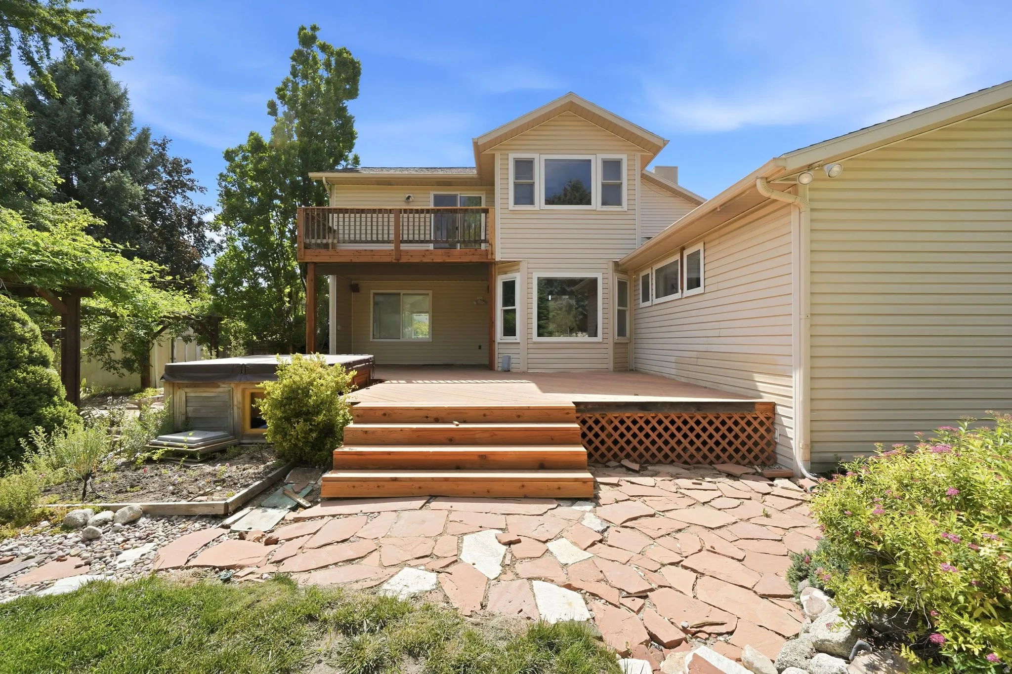 Multi-level deck with wood steps and lattice skirting, featuring an upper balcony and flagstone patio