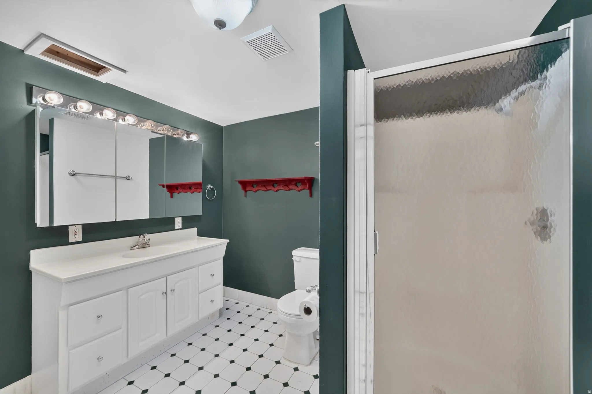 Bathroom featuring a white vanity with integrated sink, a mirrored medicine cabinet with overhead lighting, a walk-in shower with frosted glass door, a toilet, and black and white geometric tile flooring