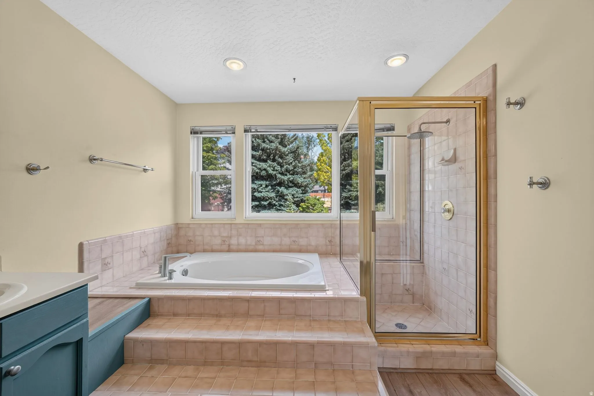 Bathroom featuring a built-in tub with tiled surround, a glass-enclosed shower with a rain shower head, and a window offering natural light
