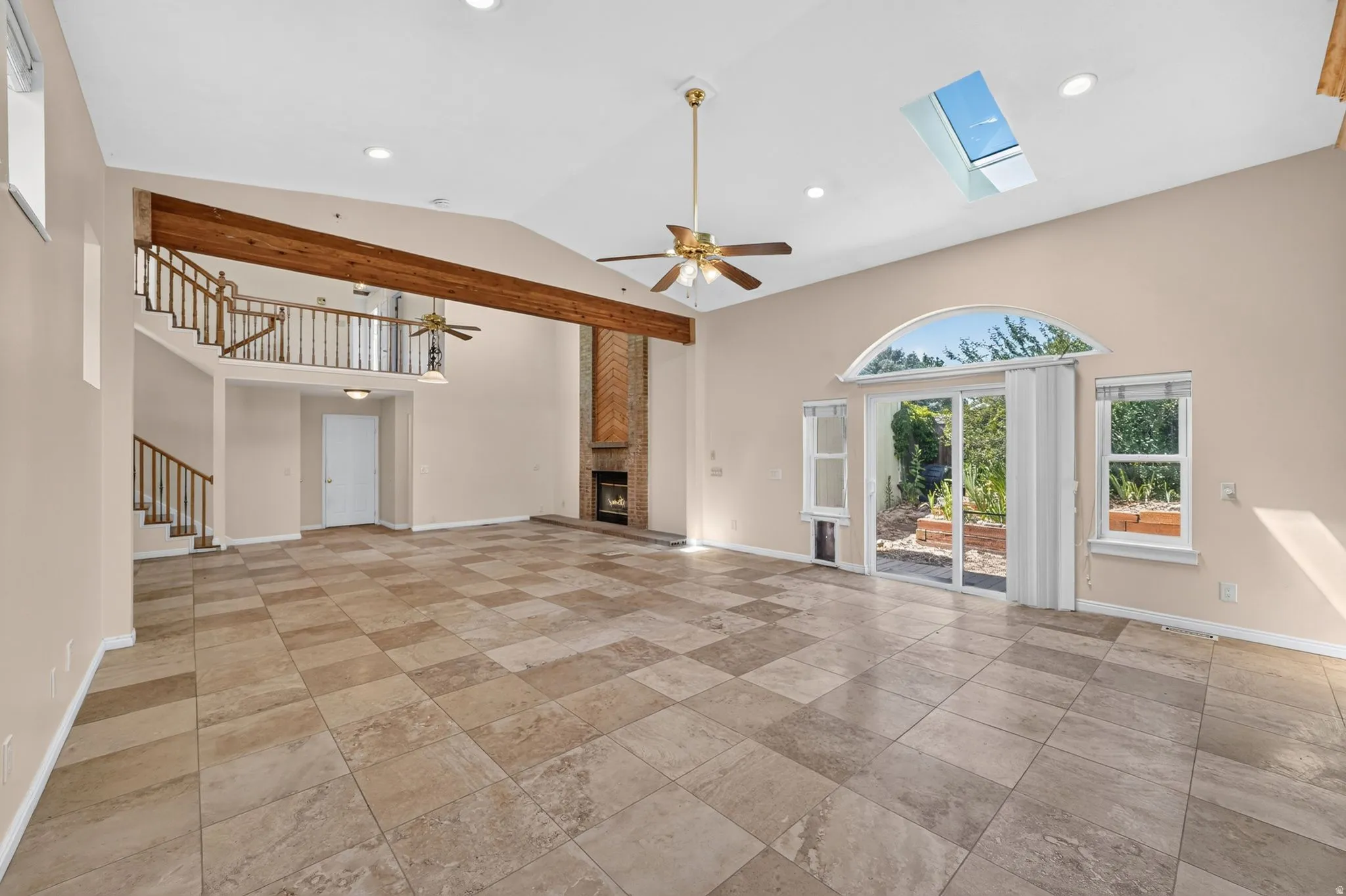 Vaulted ceiling living space featuring large format floor tiles, exposed wood beam, and a brick-faced fireplace