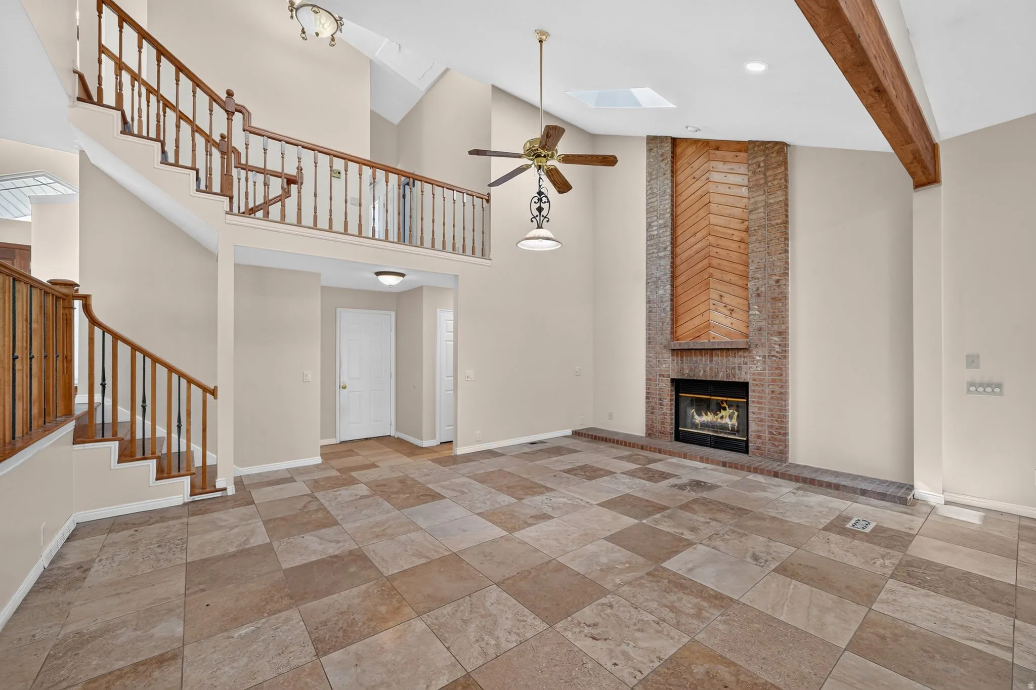 Two-story living area featuring a prominent brick fireplace with a wood accent panel, vaulted ceilings, and exposed wood beams