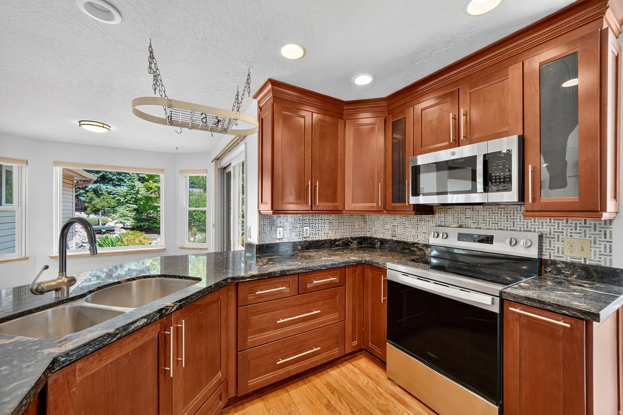 Kitchen featuring rich wood cabinetry, dark stone countertops, stainless steel appliances, and a geometric pattern tile backsplash
