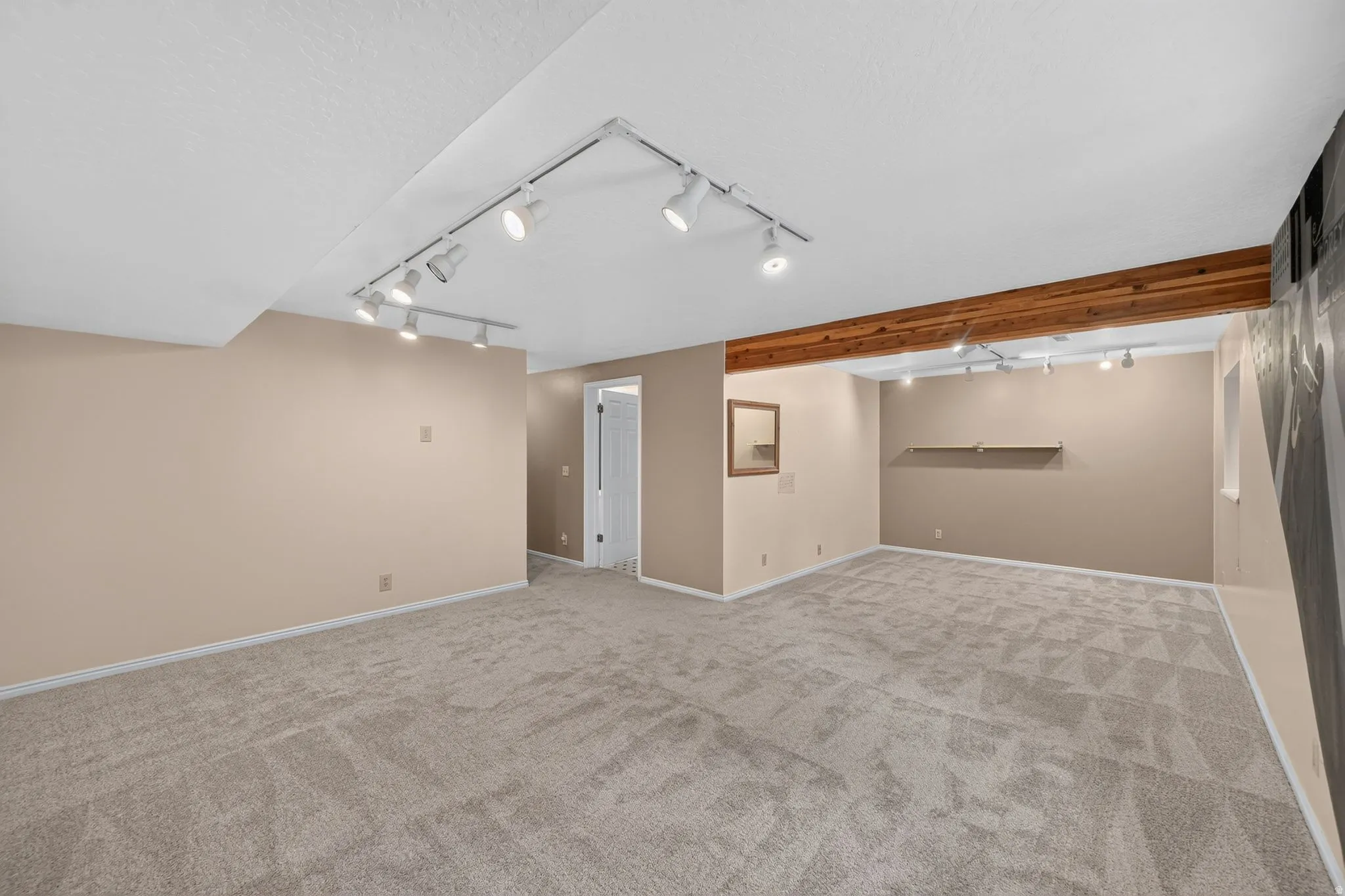 Spacious interior featuring neutral carpet, track lighting, an exposed wood beam, and light beige wall paint
