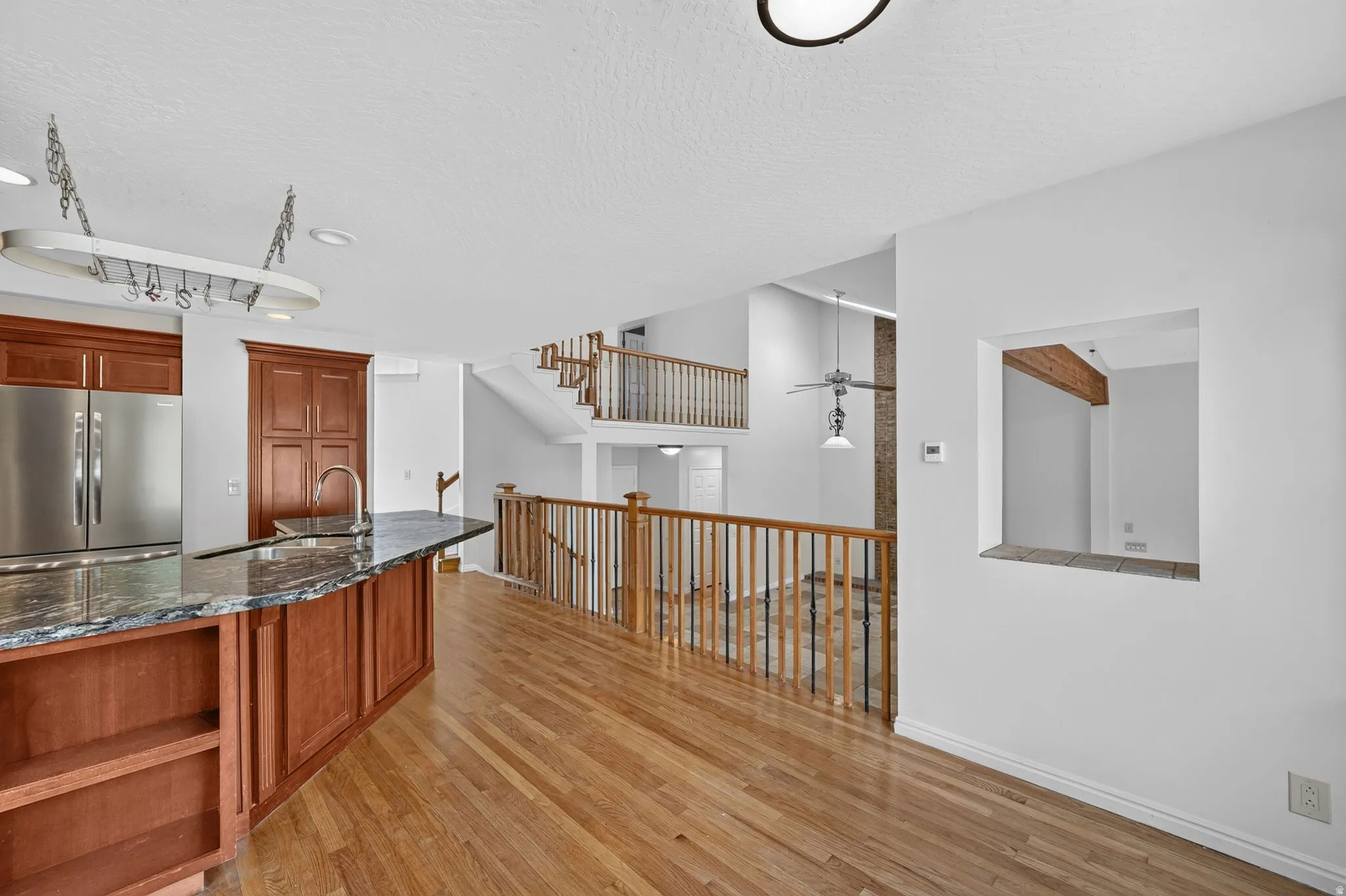 Spacious interior featuring wood-finish flooring, a kitchen island with stone countertop, stainless steel refrigerator, and wood cabinetry