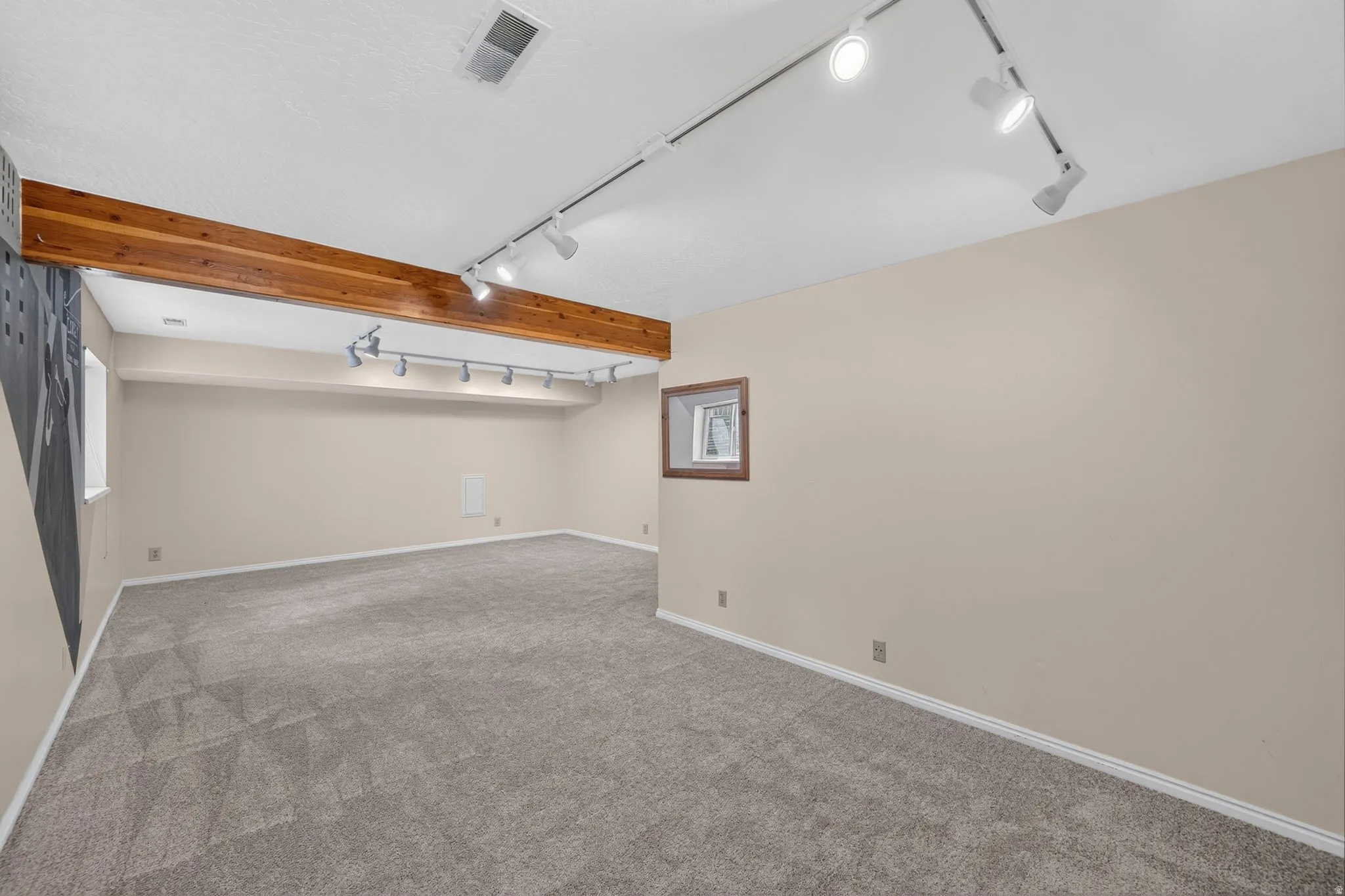 Spacious room featuring neutral carpeting, a prominent wood beam, and track lighting