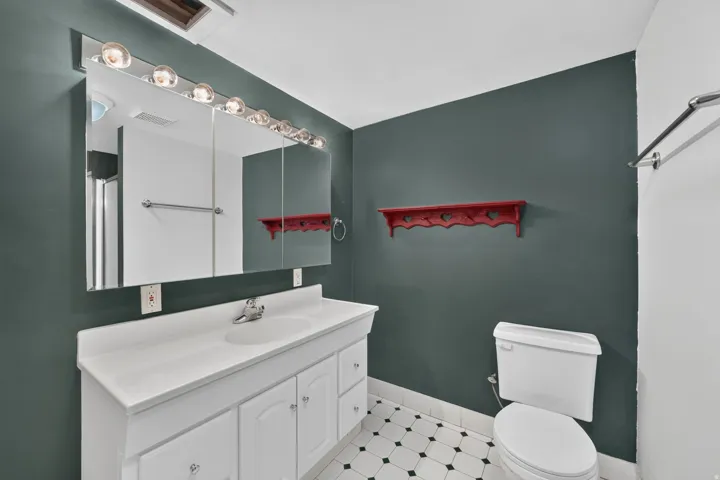Bathroom featuring a white vanity with integrated sink, a large mirrored medicine cabinet with vanity lighting, and a white toilet