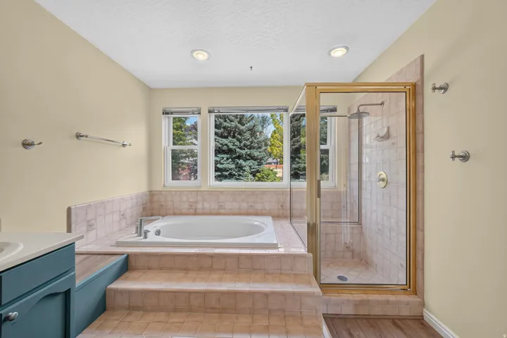 Bathroom featuring a built-in tub with tiled surround, a glass-enclosed shower with a rain shower head, and a window offering natural light