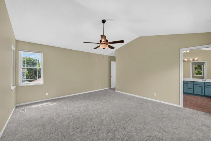 Spacious room featuring vaulted ceilings, neutral-toned walls, and grey carpeting