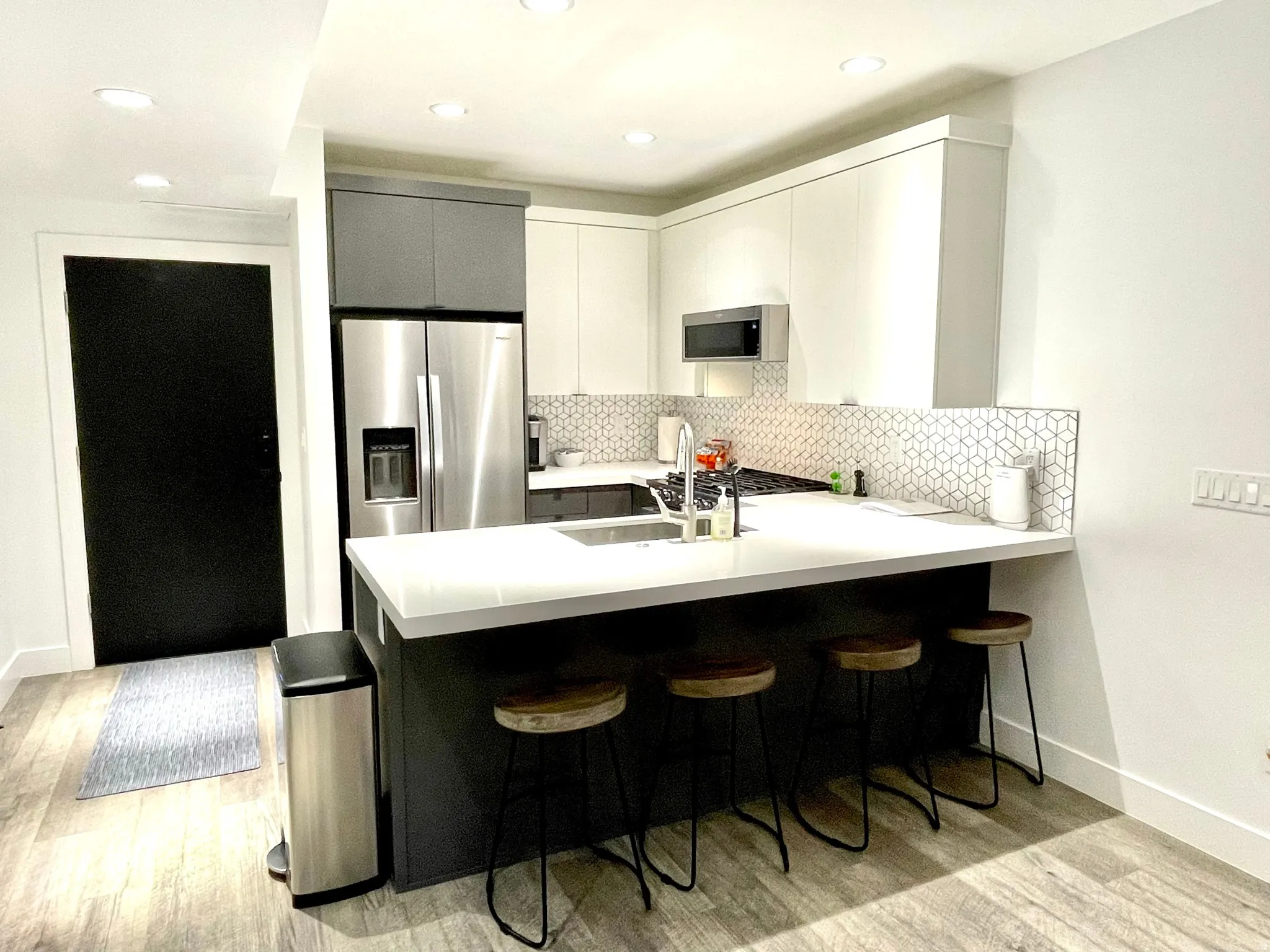 Modern kitchen featuring a white countertop island, geometric tile backsplash, stainless steel appliances, and wood-finish flooring
