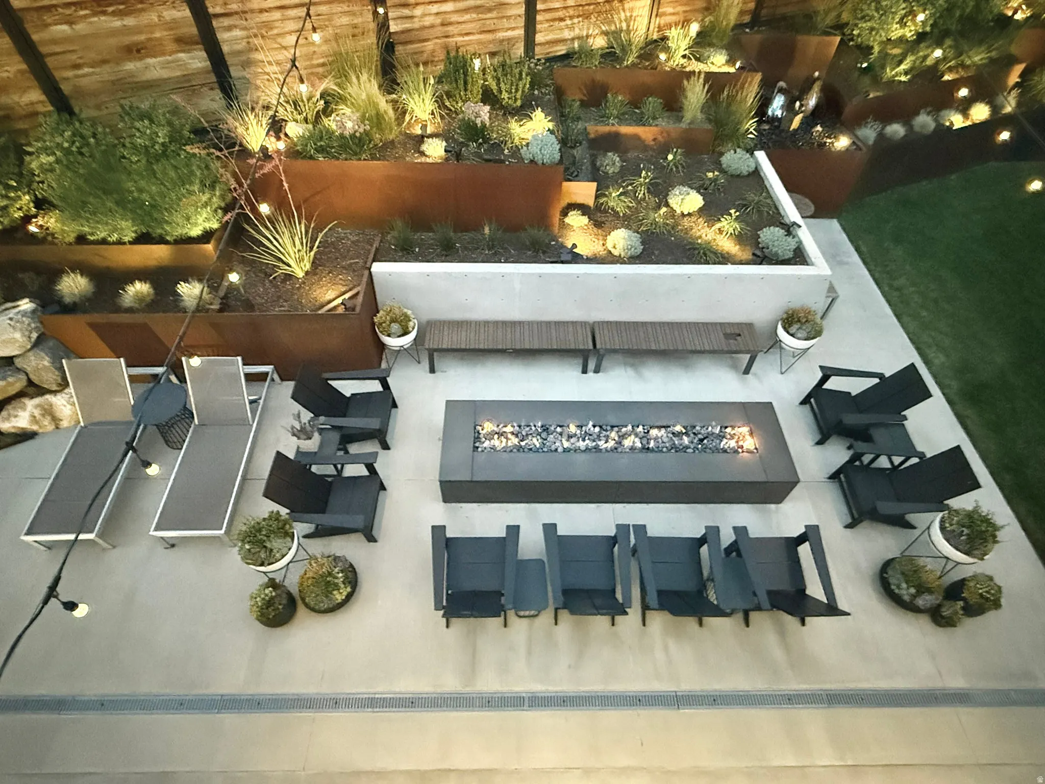 Paver patio with a built-in fire pit, surrounded by tiered planters with established landscaping and integrated lighting