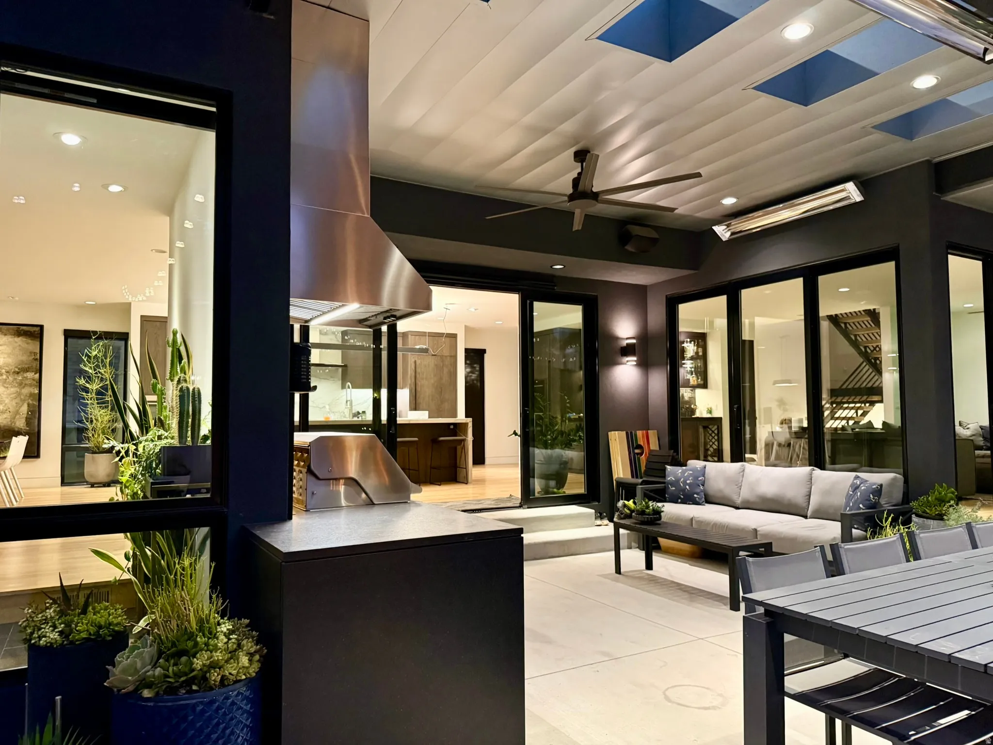 Outdoor entertaining area featuring a built-in stainless steel grill with a professional-grade hood vent, a covered patio ceiling with recessed lighting and skylights, and multiple sliding glass doors providing access to interior spaces