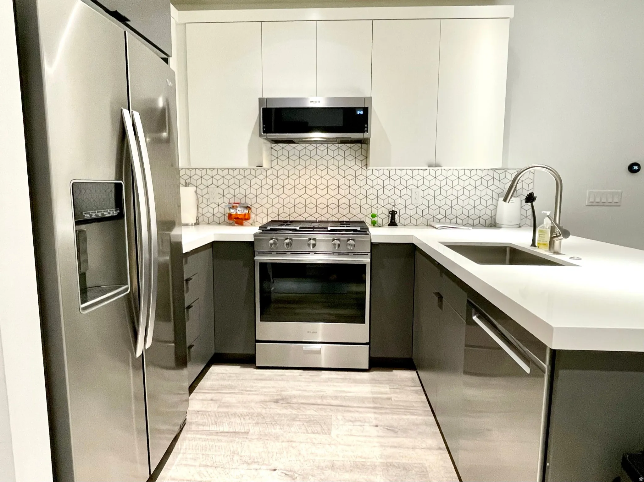 Contemporary kitchen featuring stainless steel appliances, a geometric tile backsplash, two-tone cabinetry, wood-finish flooring, and a single-basin sink with a gooseneck faucet