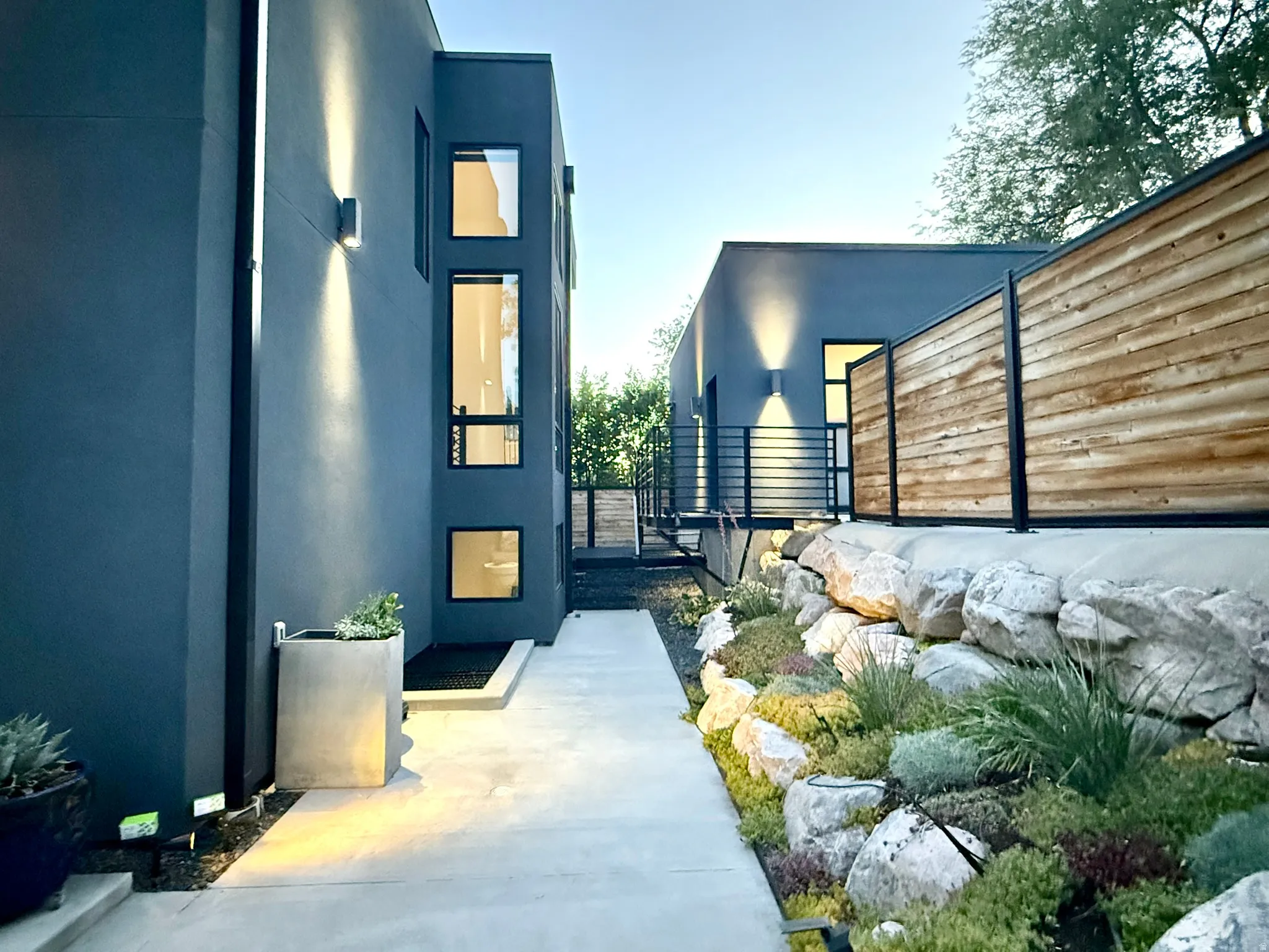 Modern architectural exterior featuring dark gray stucco, vertical rectangular windows, and contemporary outdoor lighting