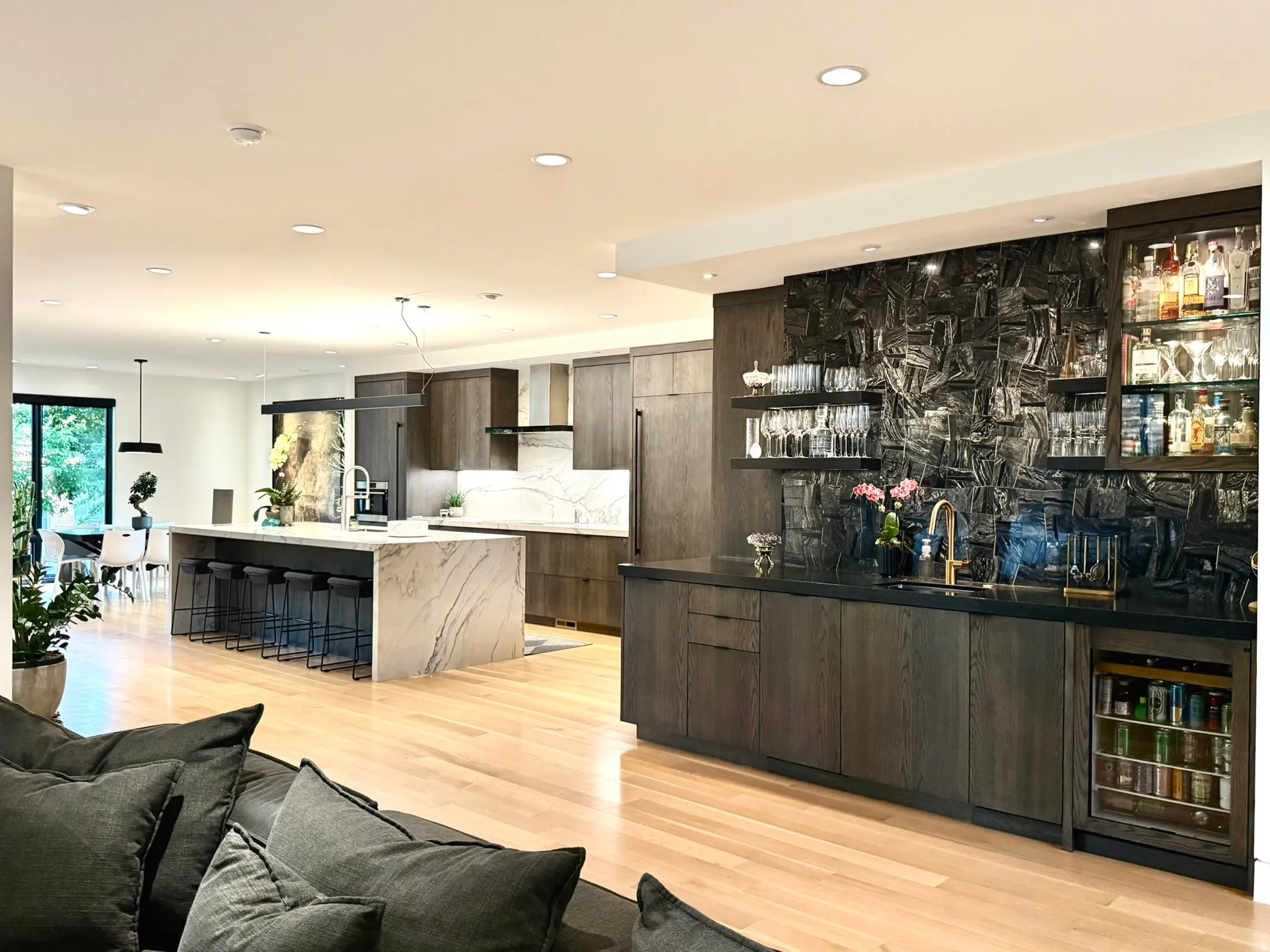 Open-concept living space with light wood-finish flooring, featuring a kitchen with a waterfall island and built-in bar area