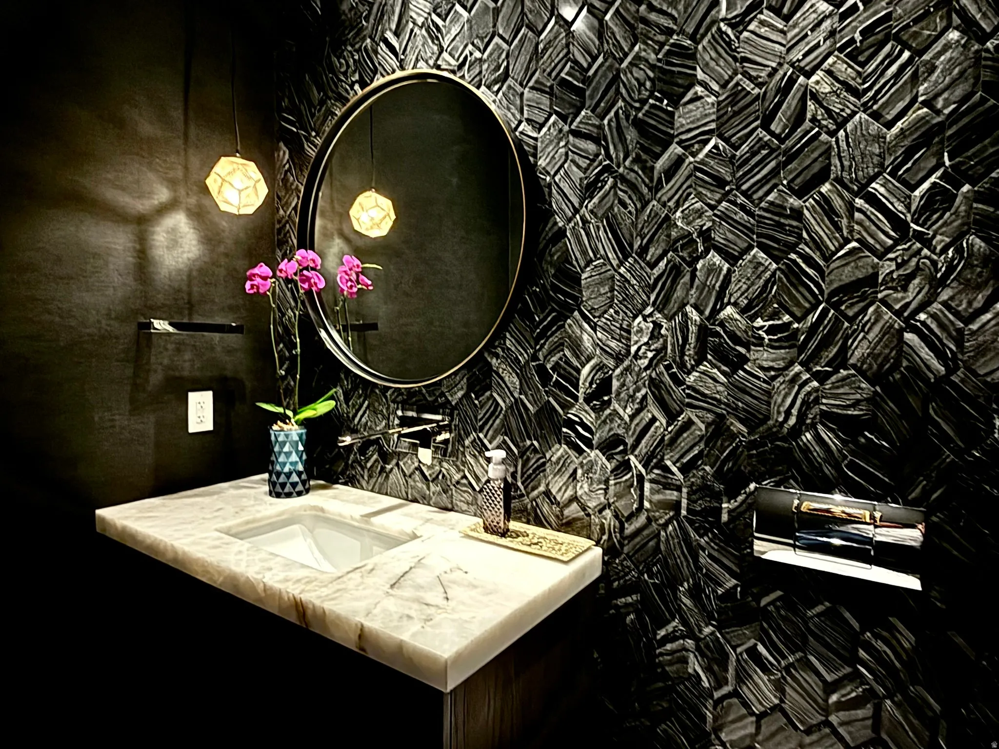Bathroom featuring a stone hexagon mosaic accent wall, wall-mounted faucet, and a rectangular undermount sink in a light-toned countertop