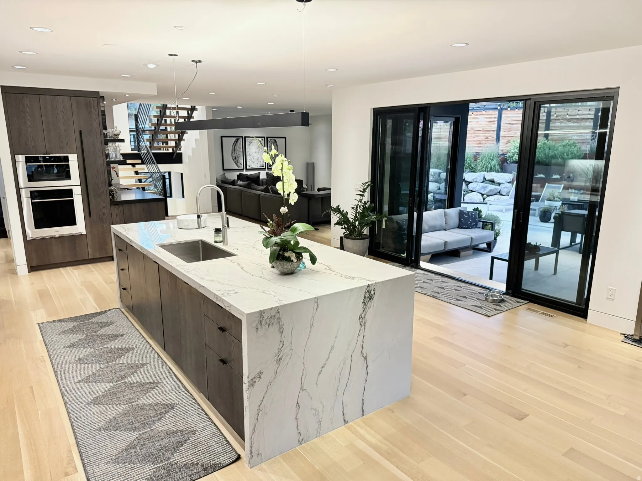 Gourmet kitchen featuring a waterfall island with integrated sink, wood-finish cabinetry, and built-in stainless steel appliances