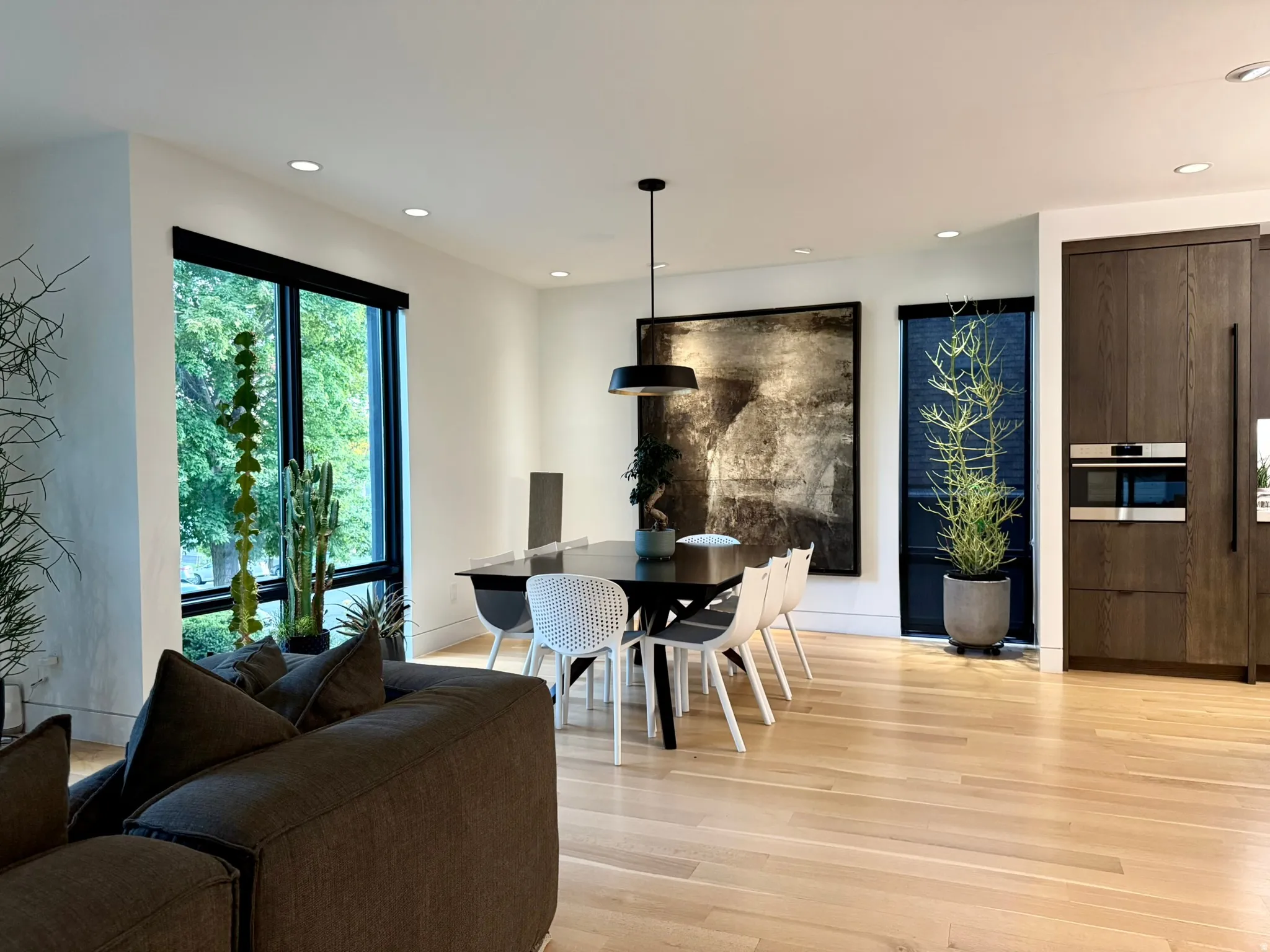 Open-concept living area featuring light wood-finish flooring, recessed lighting, expansive windows, and a built-in wall oven and microwave combination