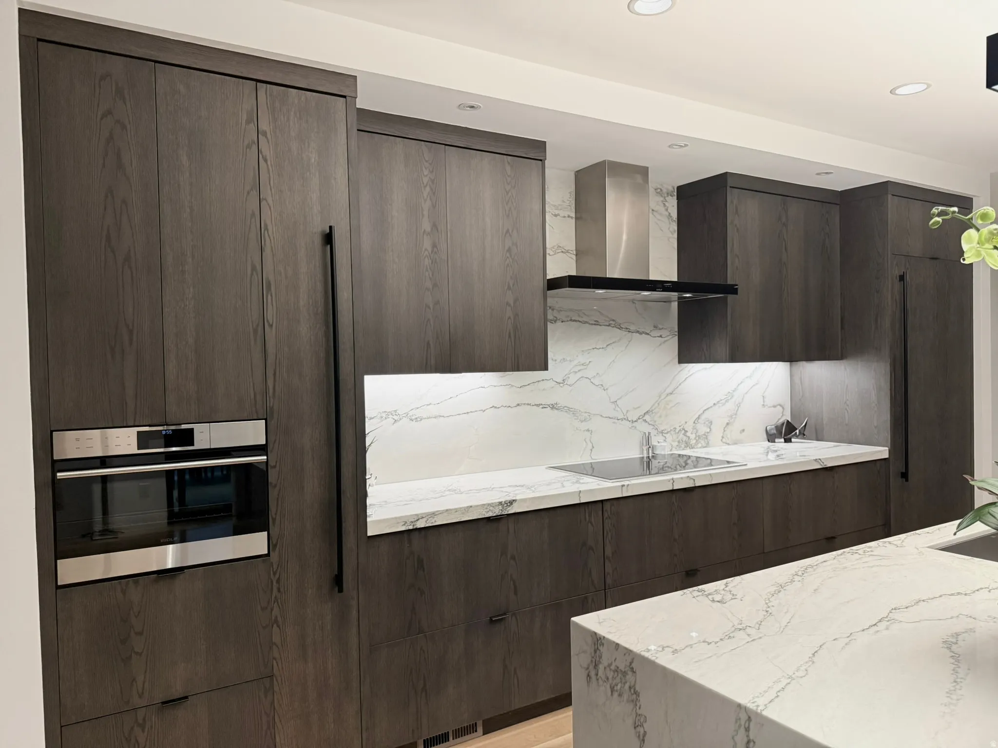 Modern kitchen featuring dark wood-finish cabinetry, integrated stainless steel appliances, and a built-in oven