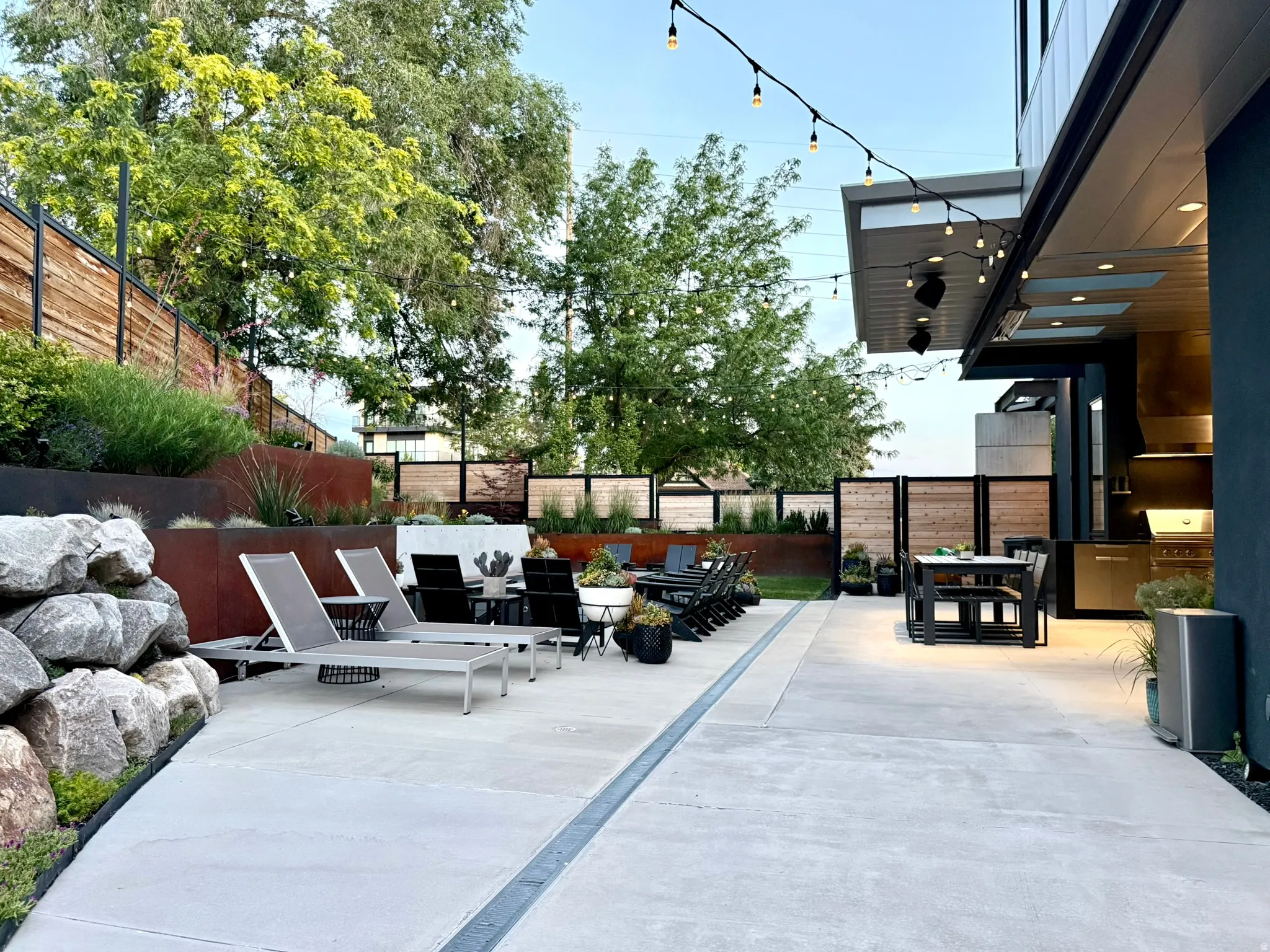 Spacious concrete patio featuring an outdoor kitchen, built-in string lighting, and extensive landscaping with terraced planters