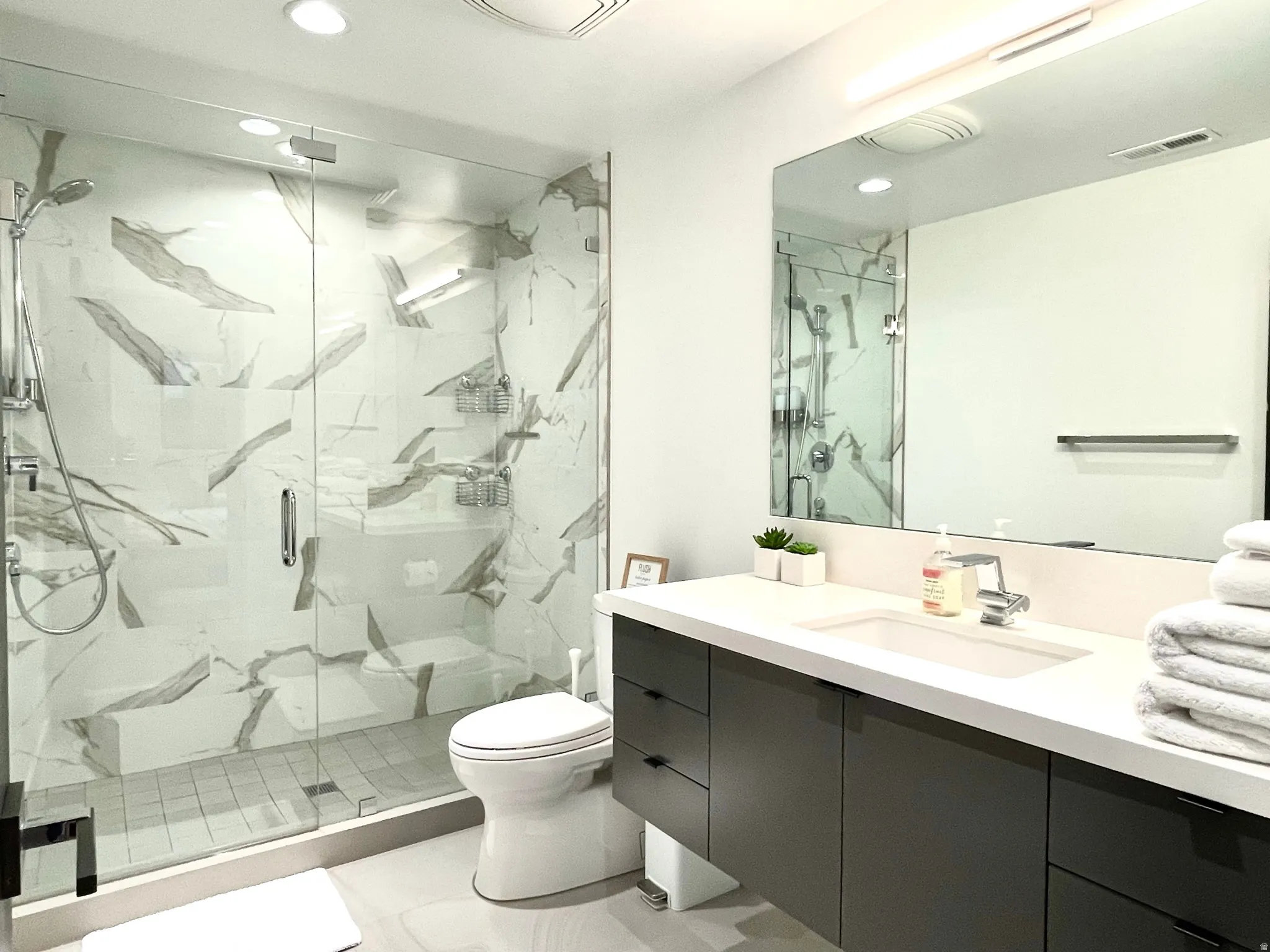 Contemporary bathroom featuring a spacious glass-enclosed shower with large format marble-patterned tile, a built-in shower bench, and a rainfall showerhead