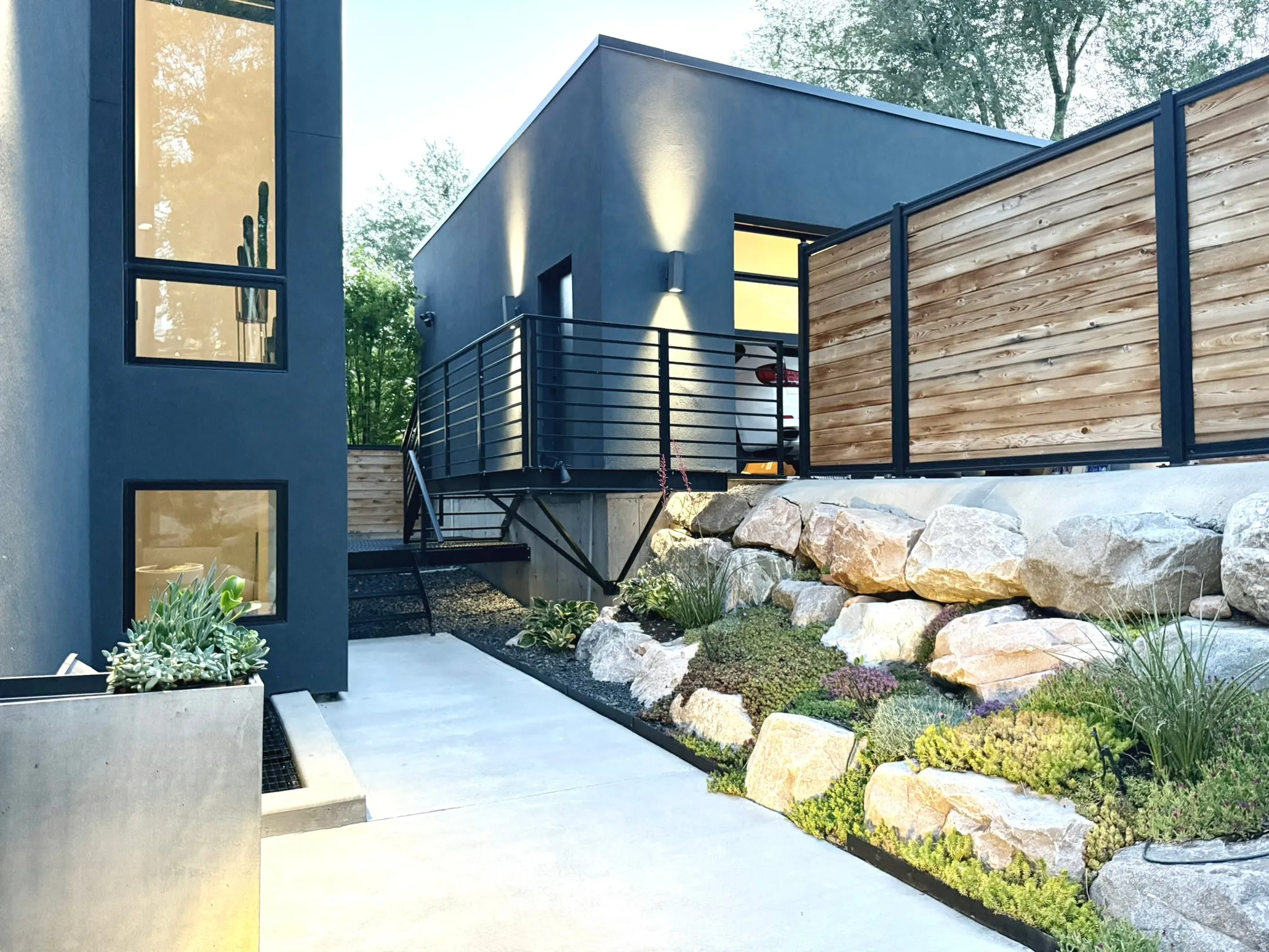 Modern architectural exterior featuring dark siding, black-framed windows, and a concrete pathway