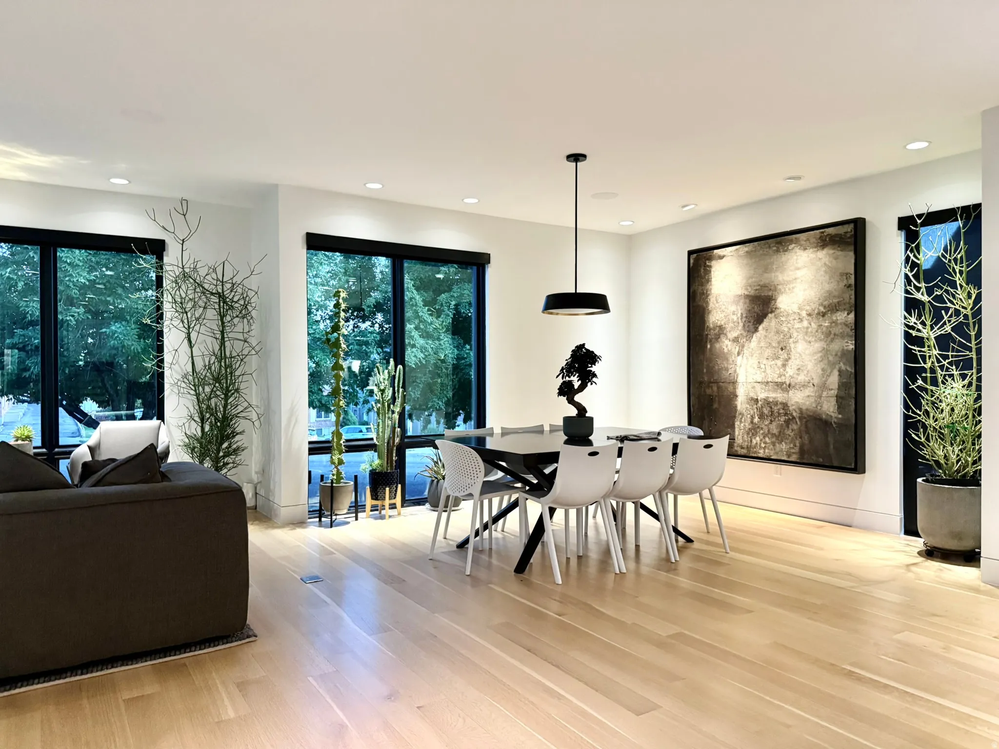 Open-concept living and dining area featuring light wood-finish flooring, recessed lighting, and large windows with dark trim