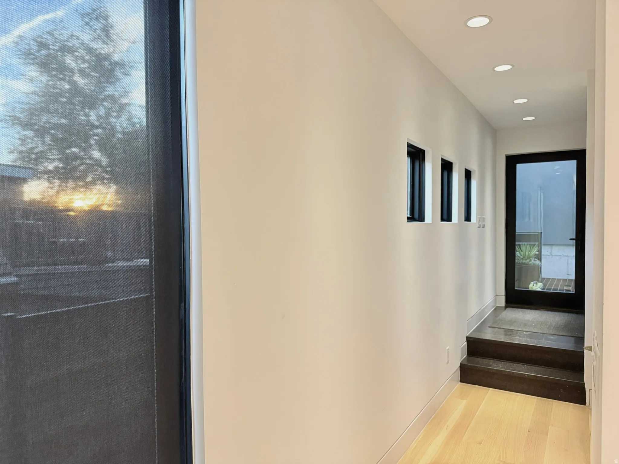 Bright interior hallway featuring light wood-finish flooring, recessed lighting, and multiple windows