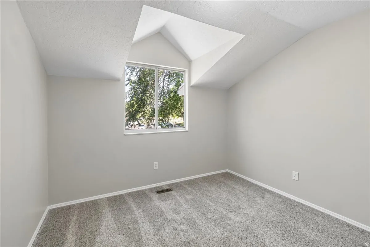 Vaulted ceiling space featuring a large window, light gray walls, and gray carpet flooring