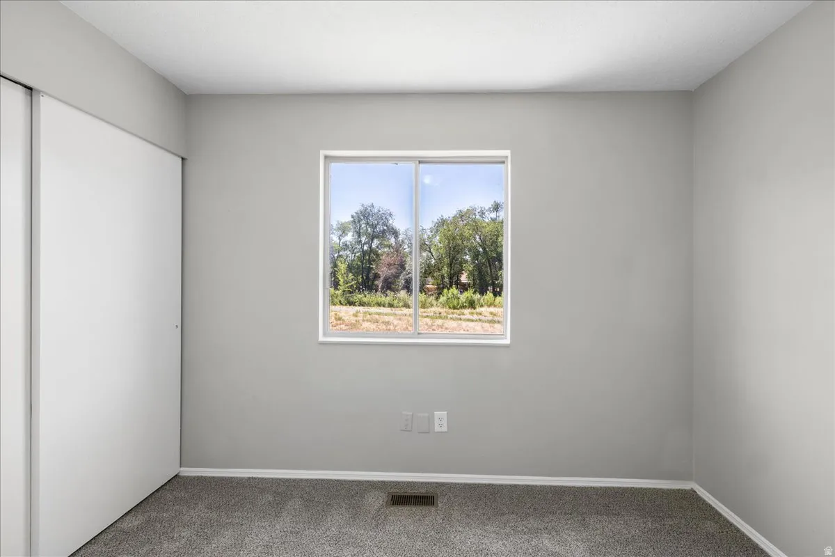 Interior room featuring neutral gray walls, a single-pane window with white trim, and a gray carpeted floor