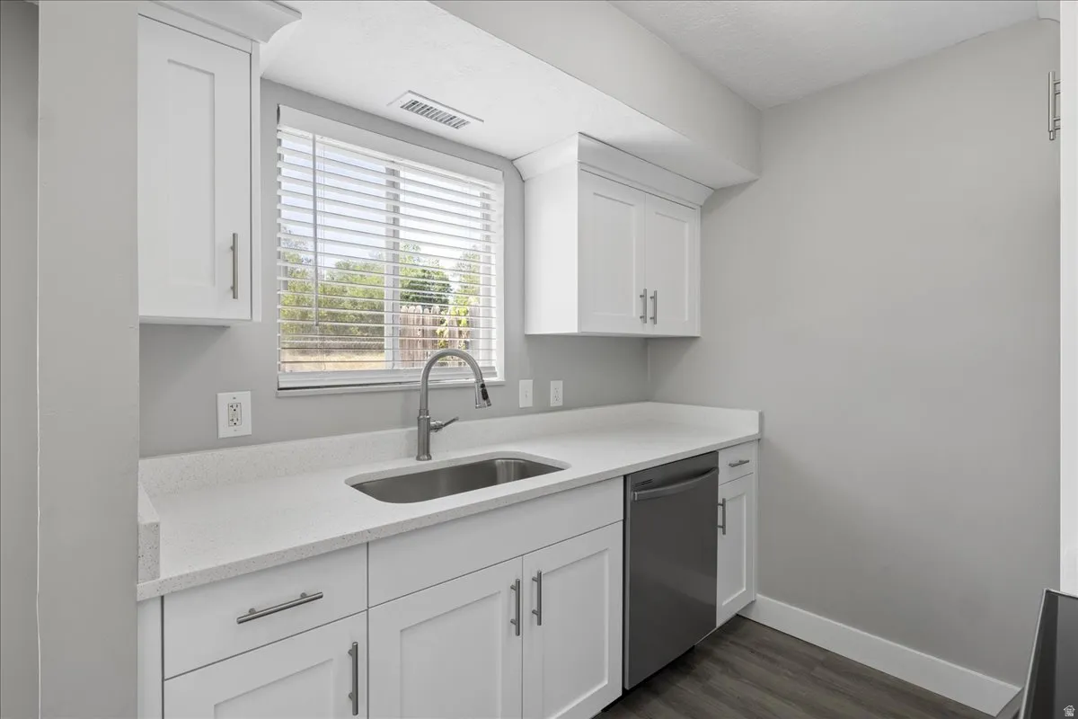 Kitchen area with white shaker cabinetry, light-toned countertops, and a stainless steel sink with a high-arc faucet