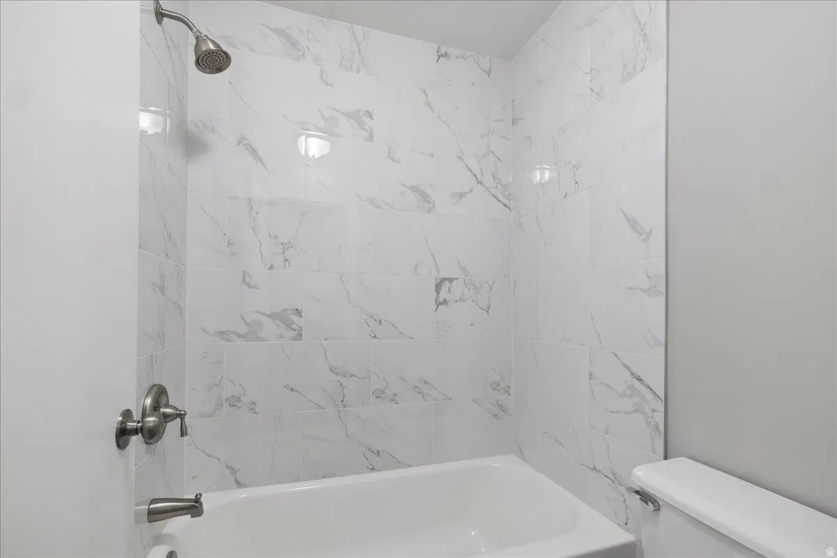 Bathroom featuring a white bathtub, white marble-look tile surround, and brushed nickel fixtures