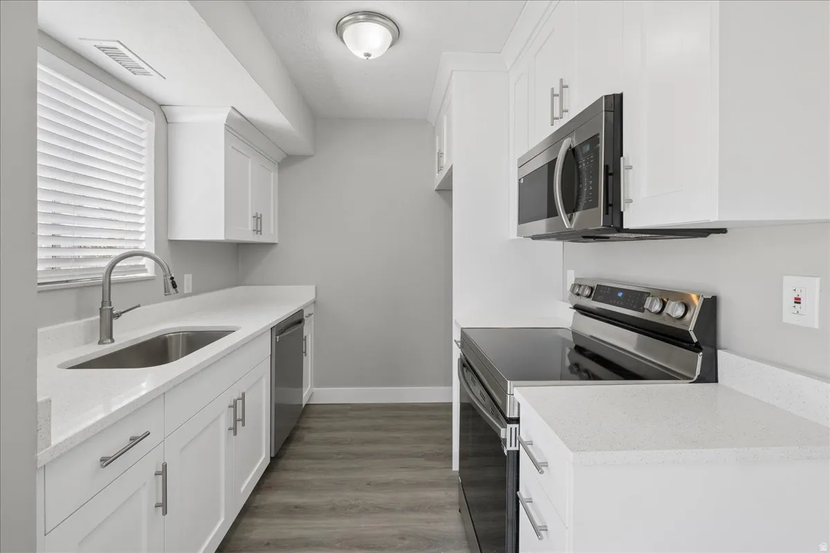Contemporary kitchen featuring white cabinetry, light countertops, stainless steel appliances, and wood-finish flooring