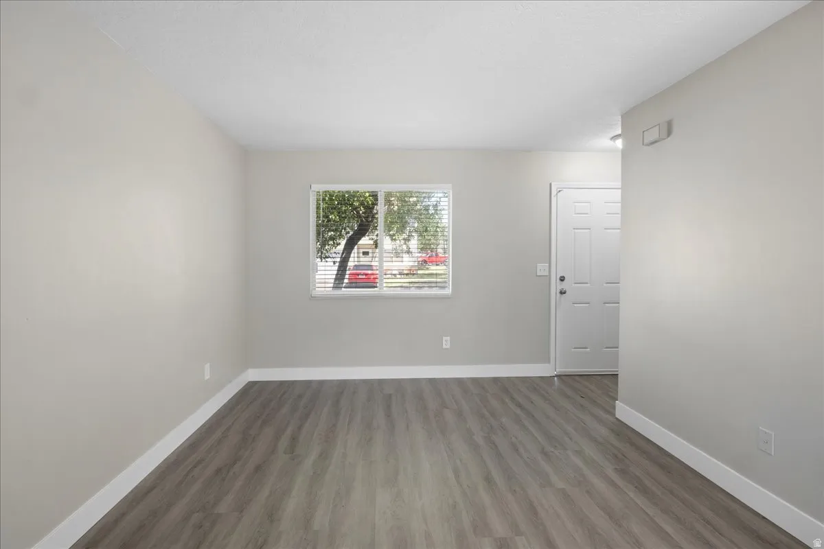 Spacious room featuring wood-finish flooring, light gray wall paint, white baseboards, and a window with blinds