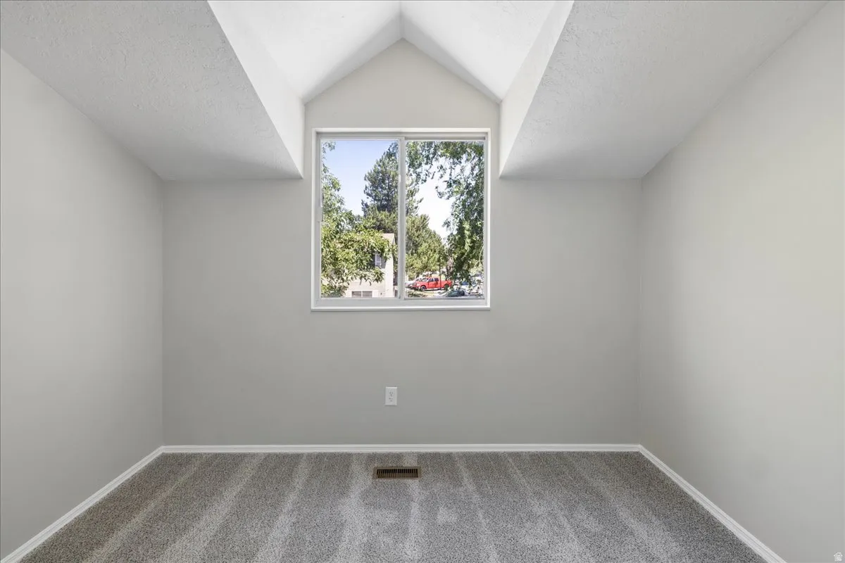Room featuring a vaulted ceiling with exposed beams, light gray walls, and new gray carpet