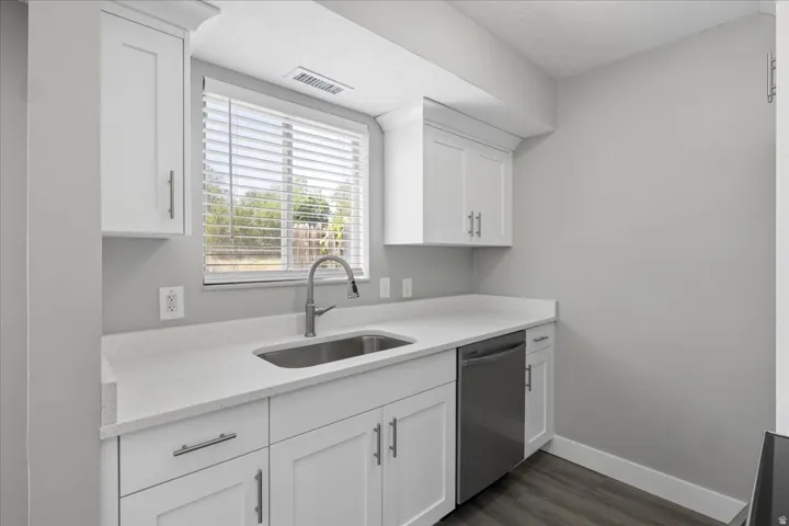 Kitchen area with white shaker cabinetry, light-toned countertops, and a stainless steel sink with a high-arc faucet