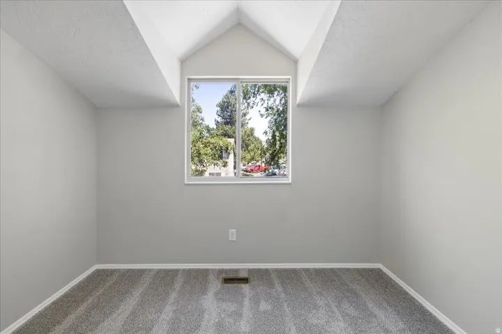 Room featuring a vaulted ceiling with exposed beams, light gray walls, and new gray carpet