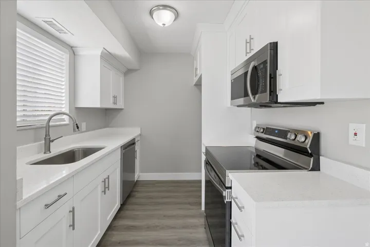 Contemporary kitchen featuring white cabinetry, light countertops, stainless steel appliances, and wood-finish flooring